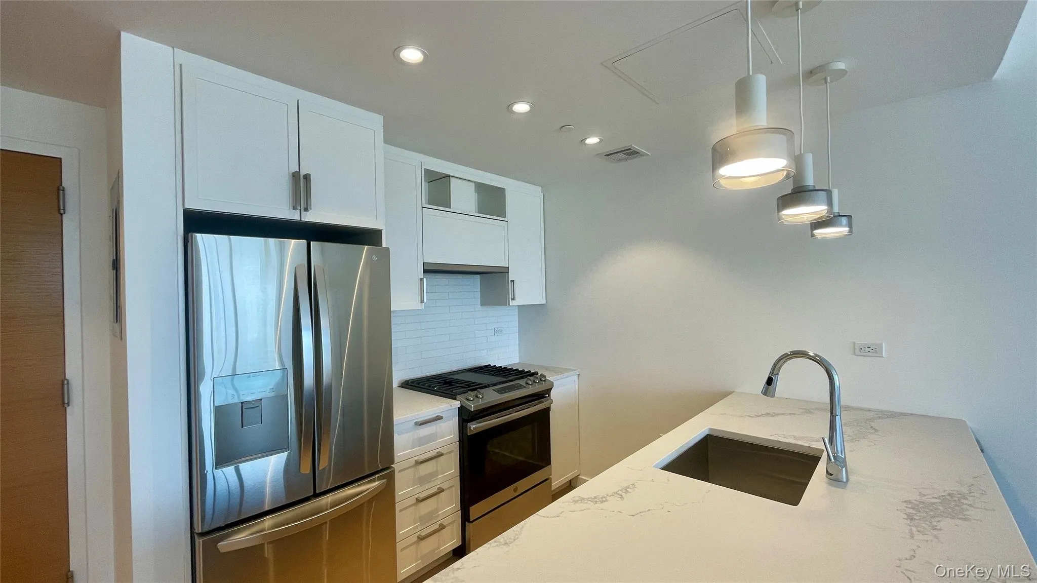 Kitchen with appliances with stainless steel finishes, backsplash, light stone countertops, pendant lighting, and white cabinets Kitchen with appliances with stainless steel finishes, backsplash, light stone countertops, pendant lighting, and white cabinets