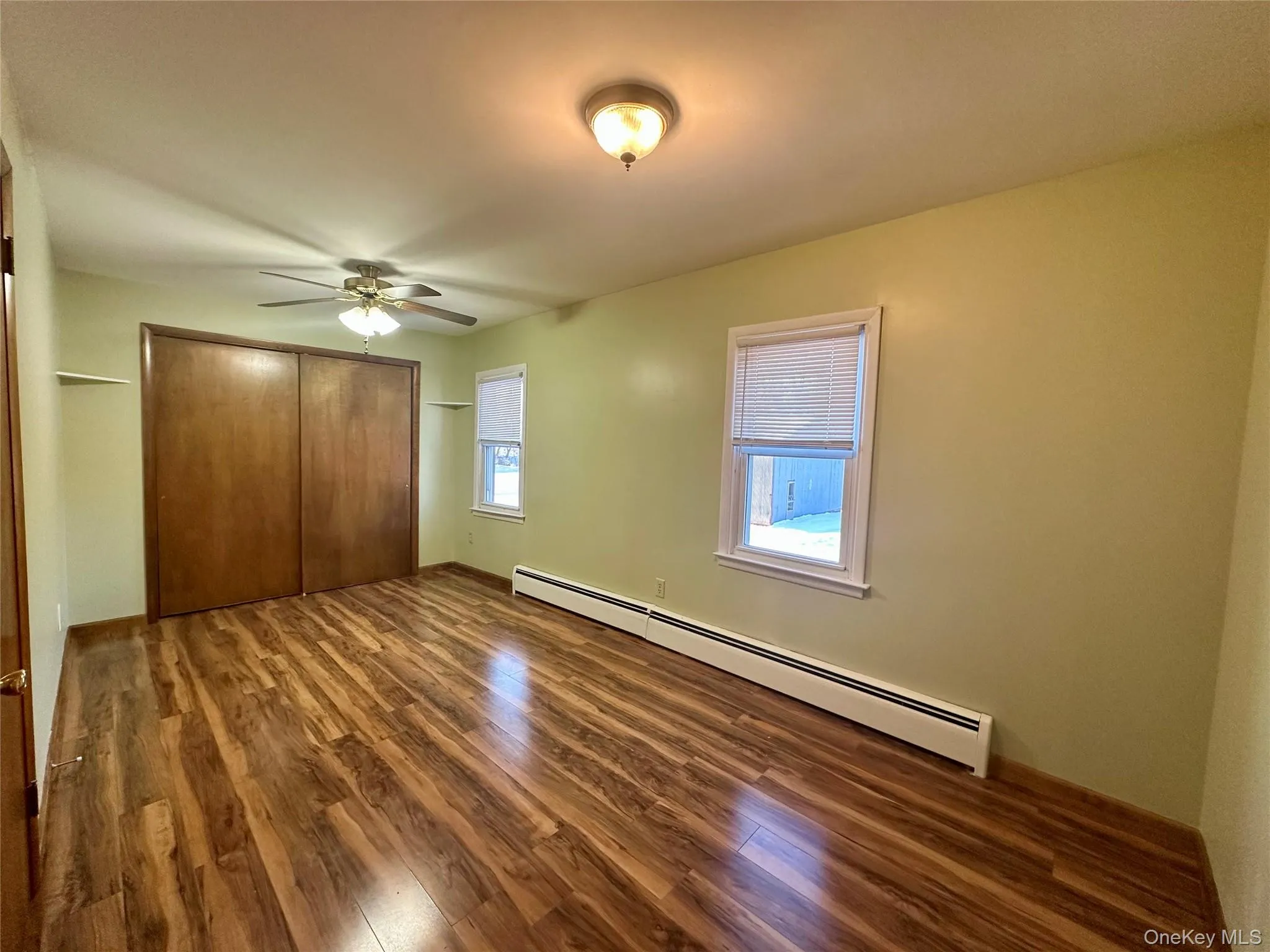 Unfurnished bedroom featuring a baseboard heating unit, dark wood-style flooring, a closet, and ceiling fan Unfurnished bedroom featuring a baseboard heating unit, dark wood-style flooring, a closet, and ceiling fan