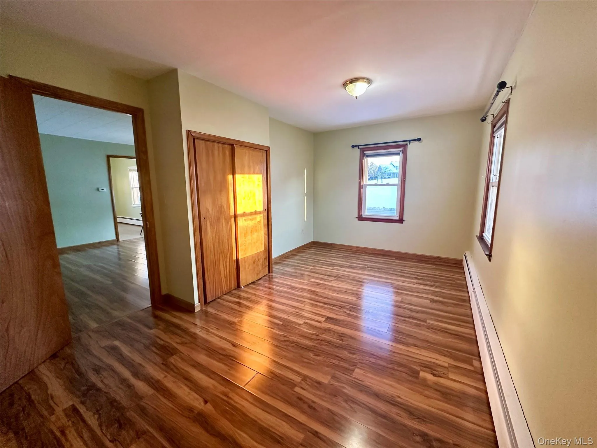 Unfurnished bedroom with a baseboard heating unit, wood finished floors, and a closet Unfurnished bedroom with a baseboard heating unit, wood finished floors, and a closet