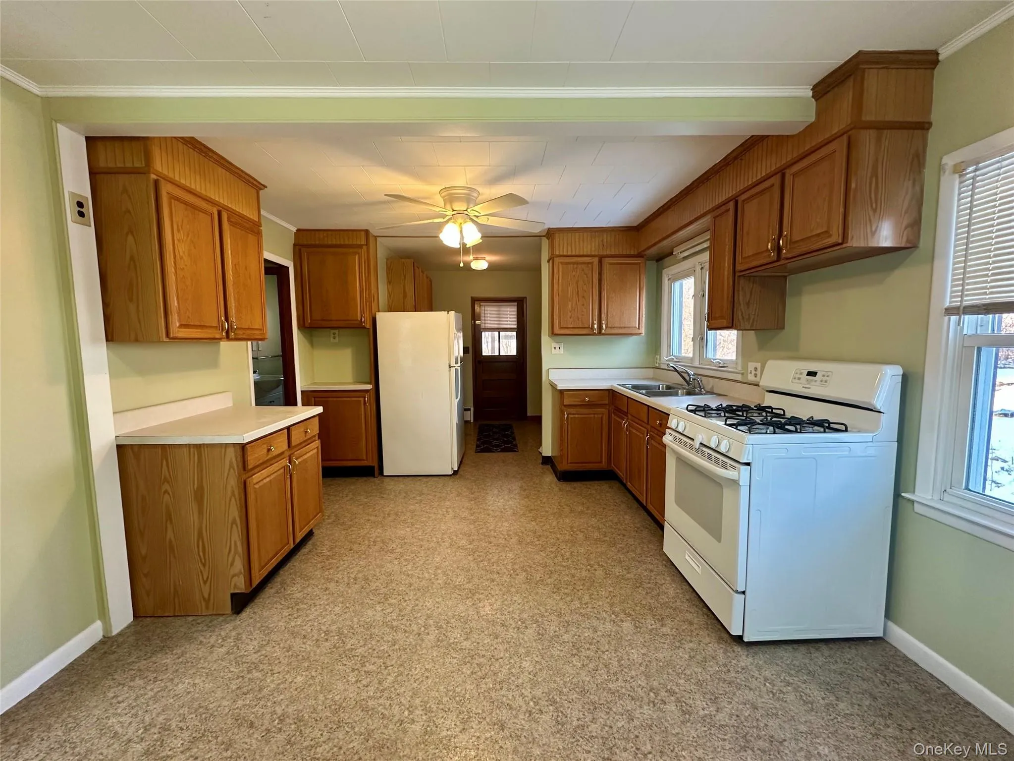 Kitchen with white appliances, light countertops, brown cabinetry, a ceiling fan, and ornamental molding Kitchen with white appliances, light countertops, brown cabinetry, a ceiling fan, and ornamental molding