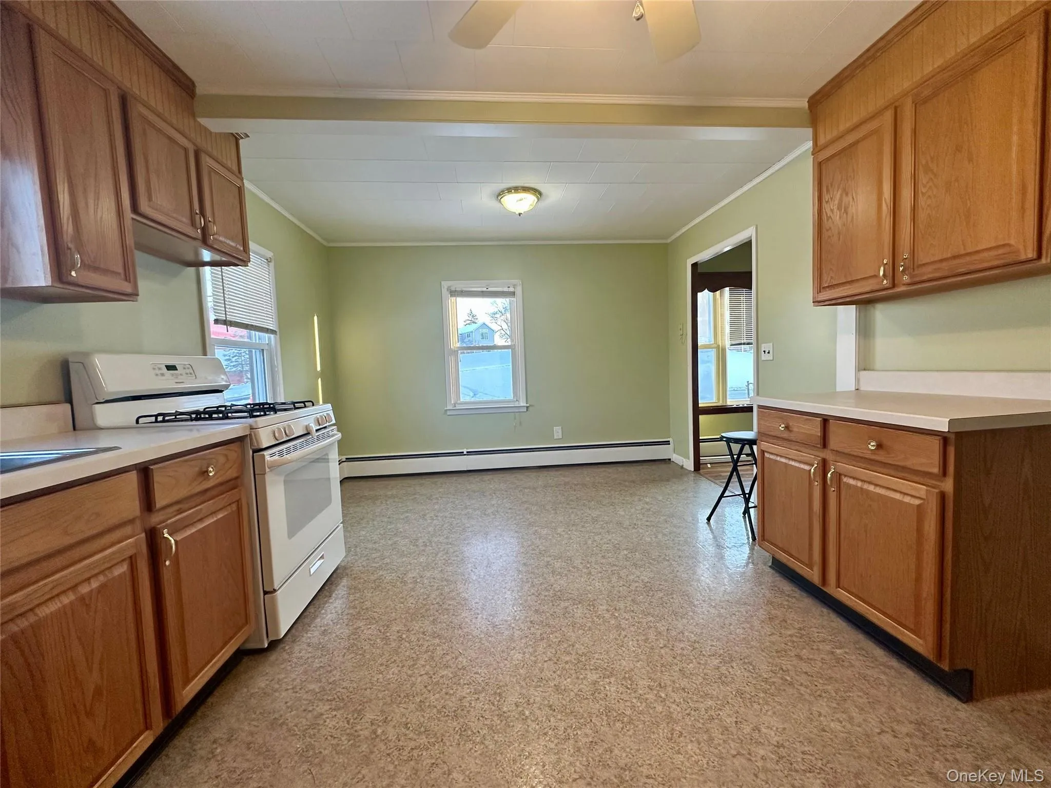 Kitchen with white range with gas stovetop, brown cabinets, light countertops, crown molding, and baseboard heating Kitchen with white range with gas stovetop, brown cabinets, light countertops, crown molding, and baseboard heating