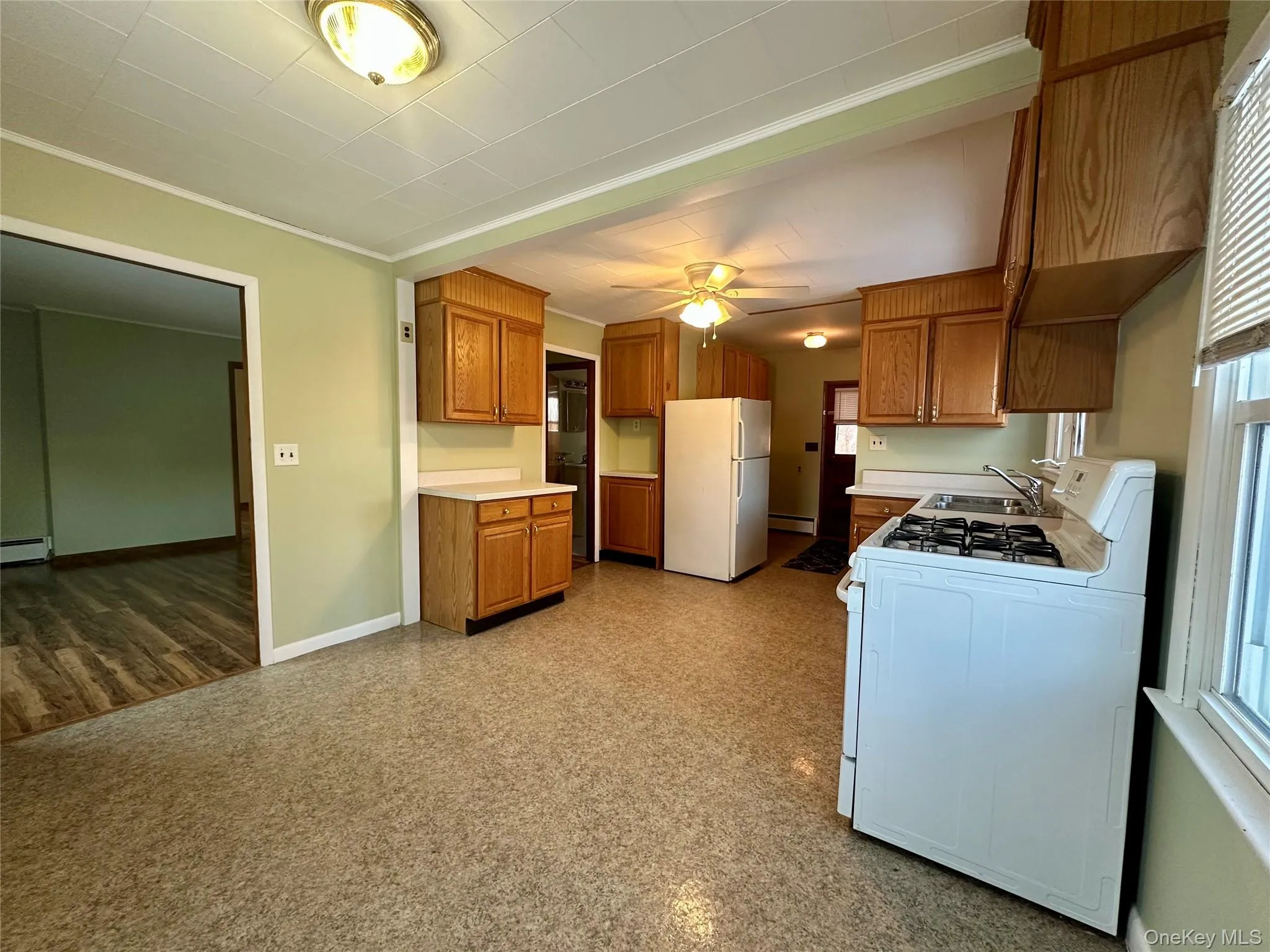 Kitchen featuring white appliances, brown cabinetry, light countertops, and crown molding Kitchen featuring white appliances, brown cabinetry, light countertops, and crown molding