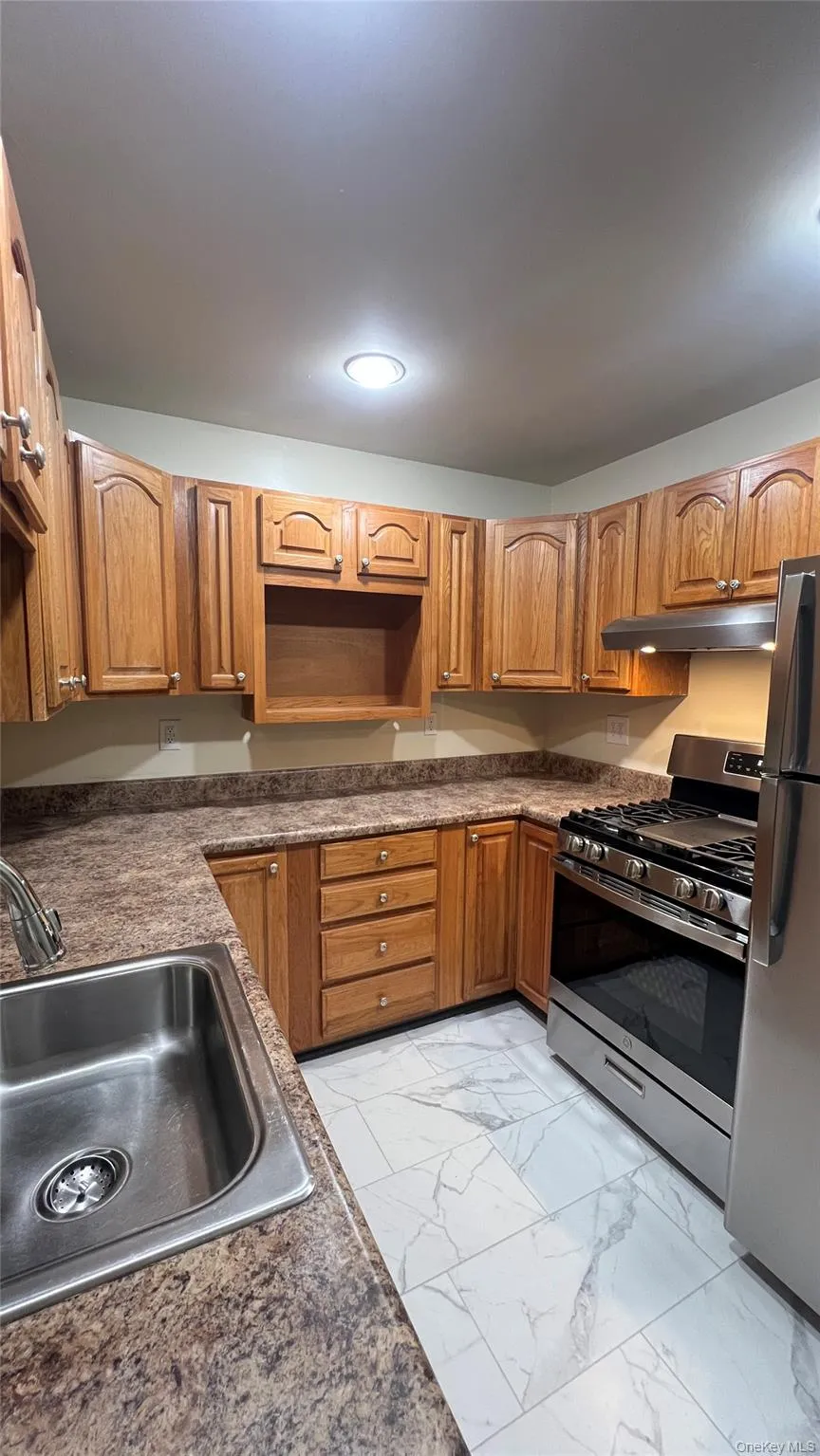 Kitchen with stainless steel appliances, brown cabinets, dark countertops, and light marble finish floors Kitchen with stainless steel appliances, brown cabinets, dark countertops, and light marble finish floors