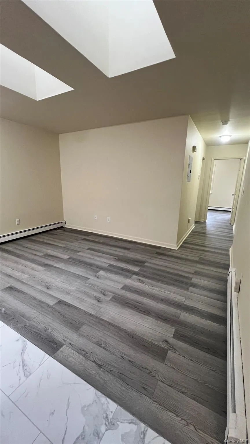 Living room with a skylight, finish flooring, and a baseboard heating unit Living room with a skylight, finish flooring, and a baseboard heating unit