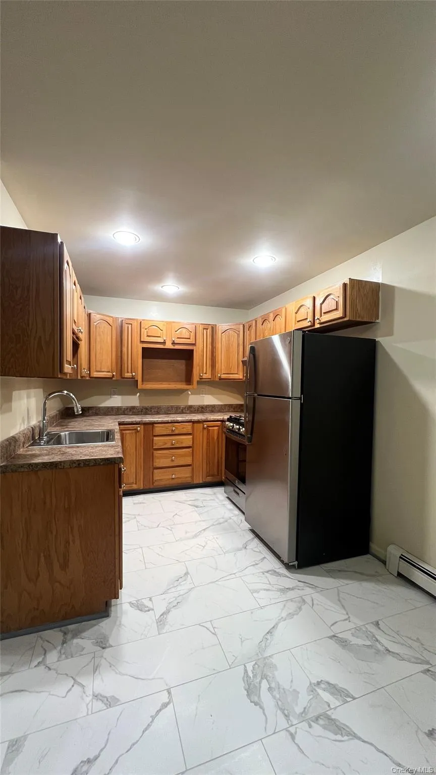 Kitchen featuring appliances with stainless steel finishes, dark countertops, light marble finish flooring, brown cabinets, and recessed lighting Kitchen featuring appliances with stainless steel finishes, dark countertops, light marble finish flooring, brown cabinets, and recessed lighting