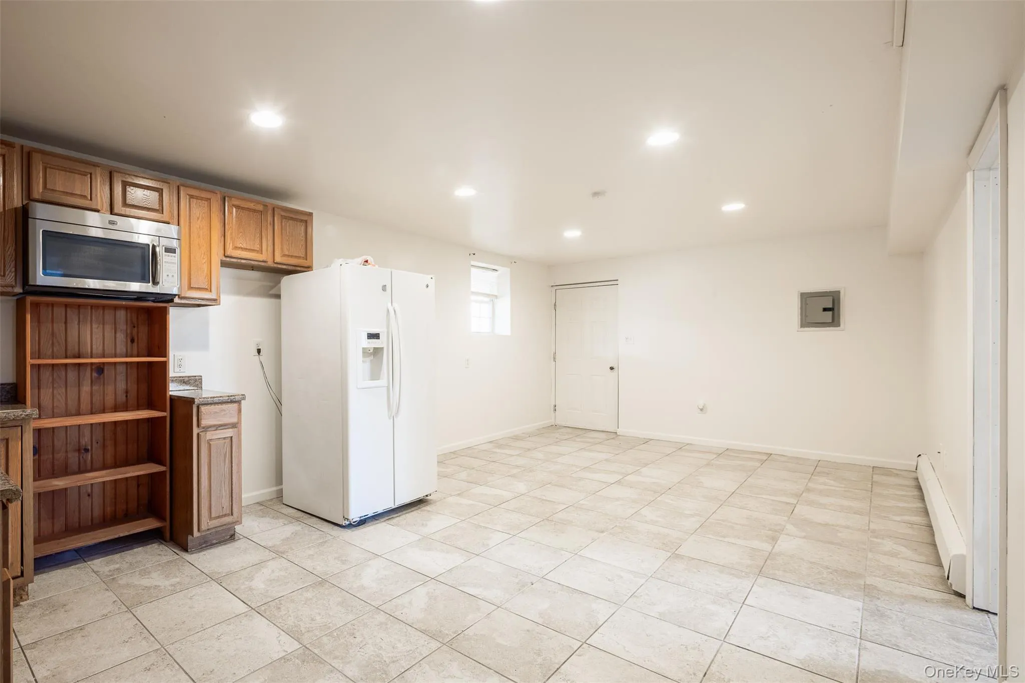 Kitchen featuring recessed lighting, white fridge with ice dispenser, brown cabinets, stainless steel microwave, and baseboard heating Kitchen featuring recessed lighting, white fridge with ice dispenser, brown cabinets, stainless steel microwave, and baseboard heating