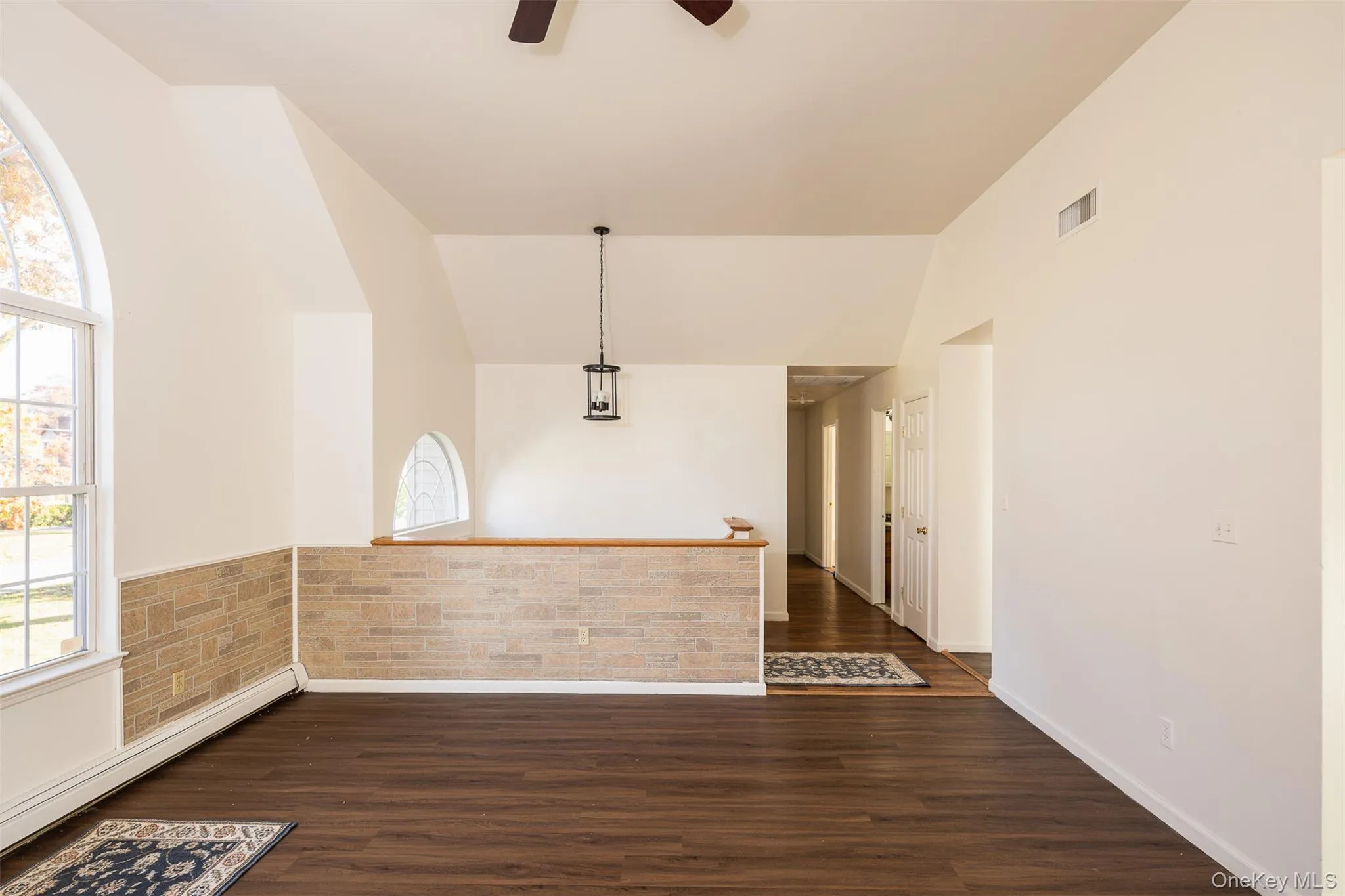 Unfurnished room featuring vaulted ceiling, baseboard heating, dark wood finished floors, and a ceiling fan Unfurnished room featuring vaulted ceiling, baseboard heating, dark wood finished floors, and a ceiling fan