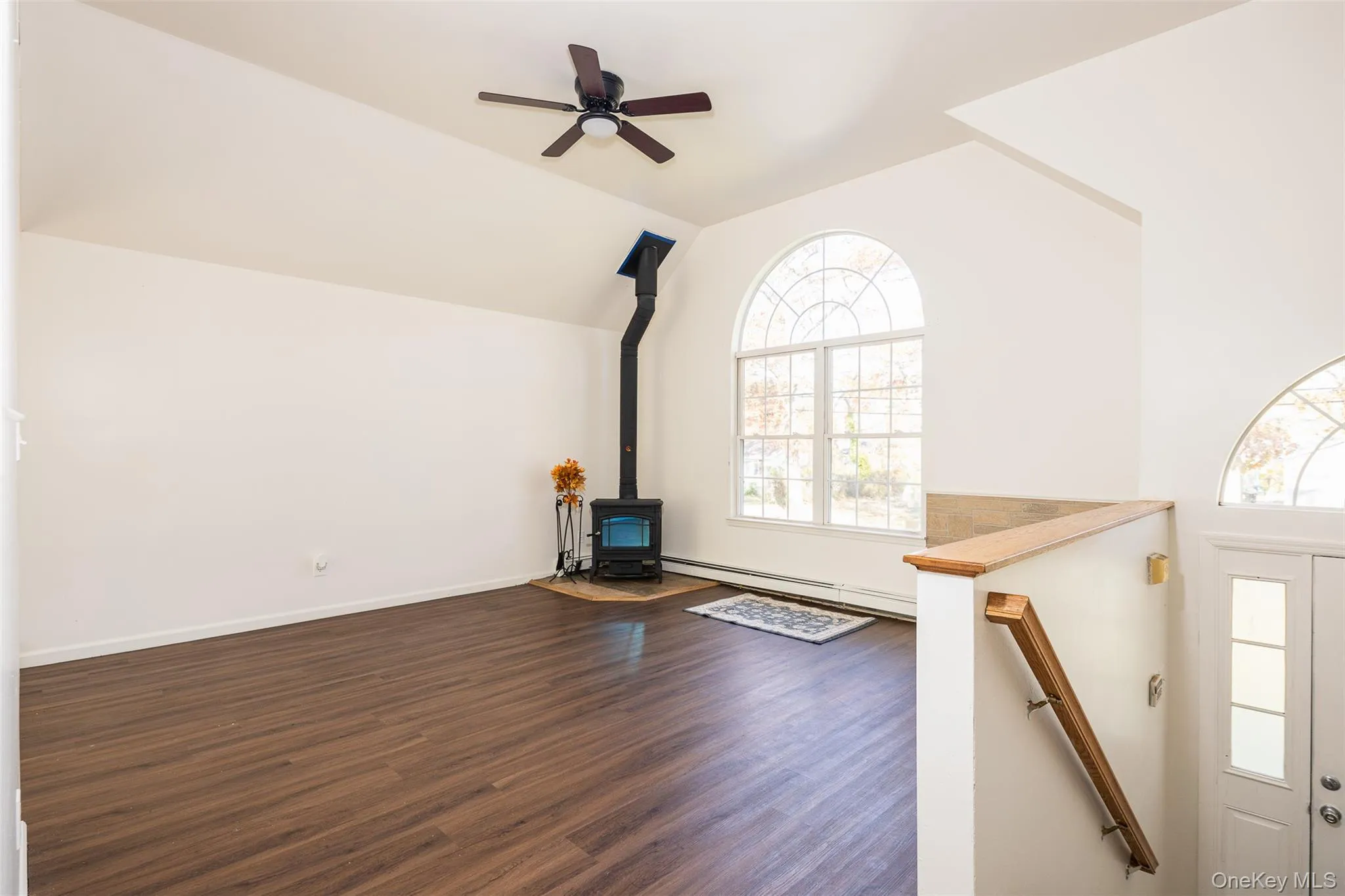Unfurnished living room featuring a wood stove, dark wood-style flooring, lofted ceiling, and ceiling fan Unfurnished living room featuring a wood stove, dark wood-style flooring, lofted ceiling, and ceiling fan