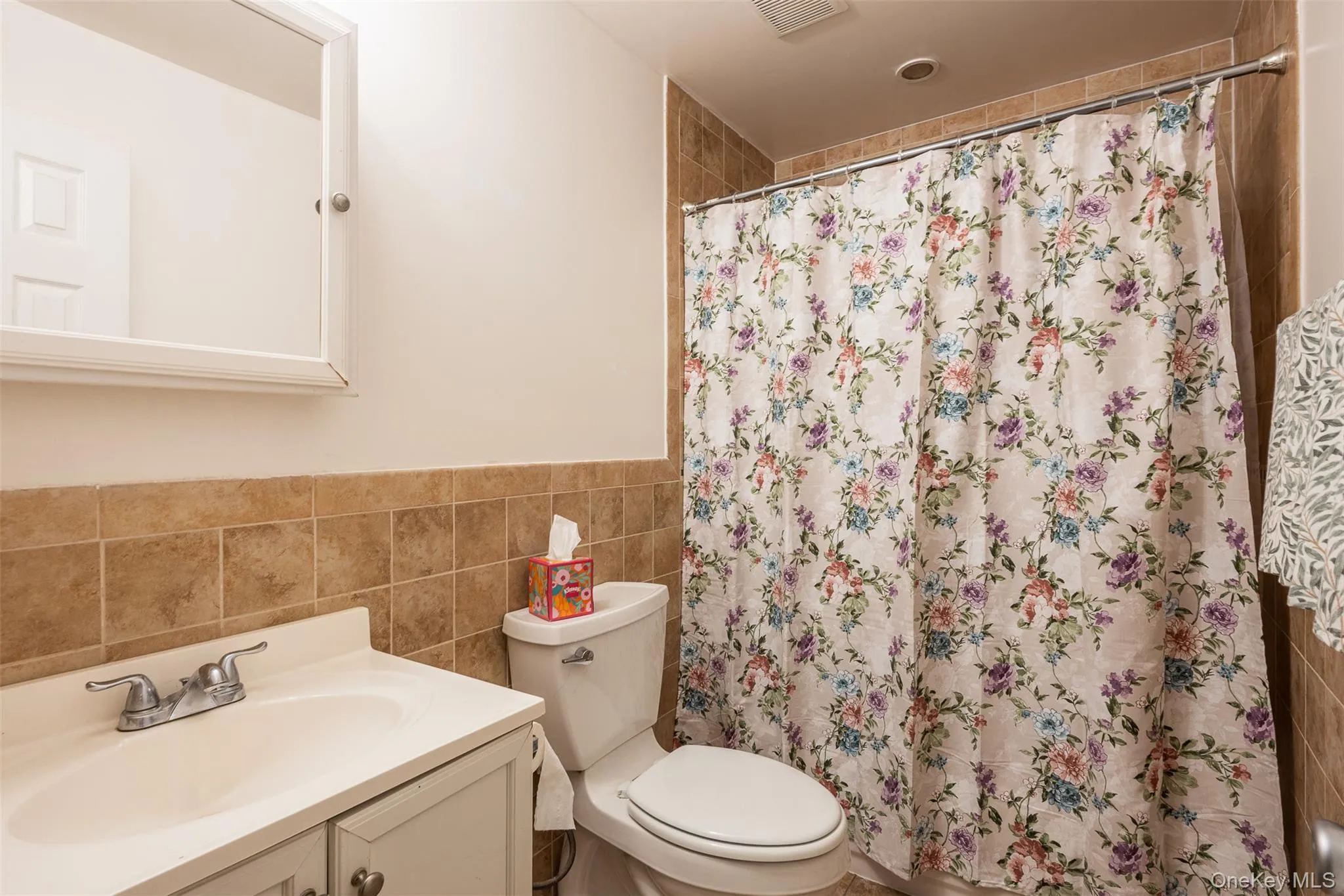 Bathroom featuring tile walls, vanity, a shower with shower curtain, and a wainscoted wall Bathroom featuring tile walls, vanity, a shower with shower curtain, and a wainscoted wall