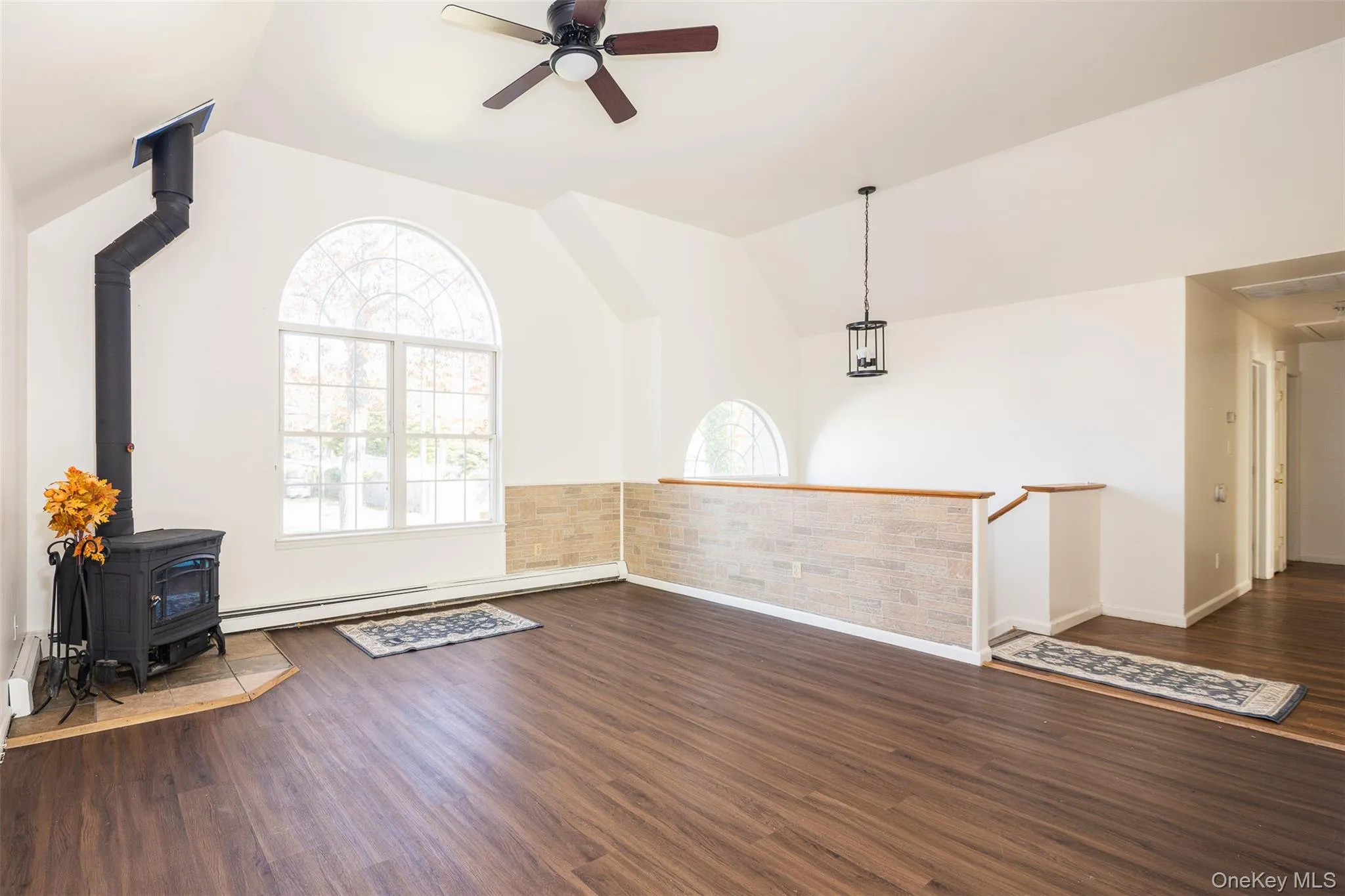 Unfurnished living room featuring a wood stove, plenty of natural light, dark wood-style floors, and lofted ceiling Unfurnished living room featuring a wood stove, plenty of natural light, dark wood-style floors, and lofted ceiling