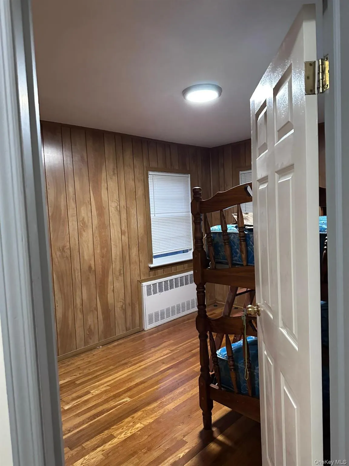 Bedroom with wood finished floors, wooden walls, and radiator heating unit Bedroom with wood finished floors, wooden walls, and radiator heating unit