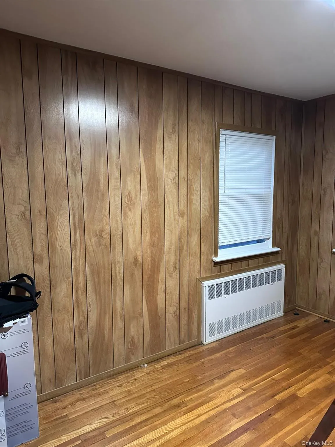 Unfurnished room with radiator heating unit, wood finished floors, and wood walls Unfurnished room with radiator heating unit, wood finished floors, and wood walls