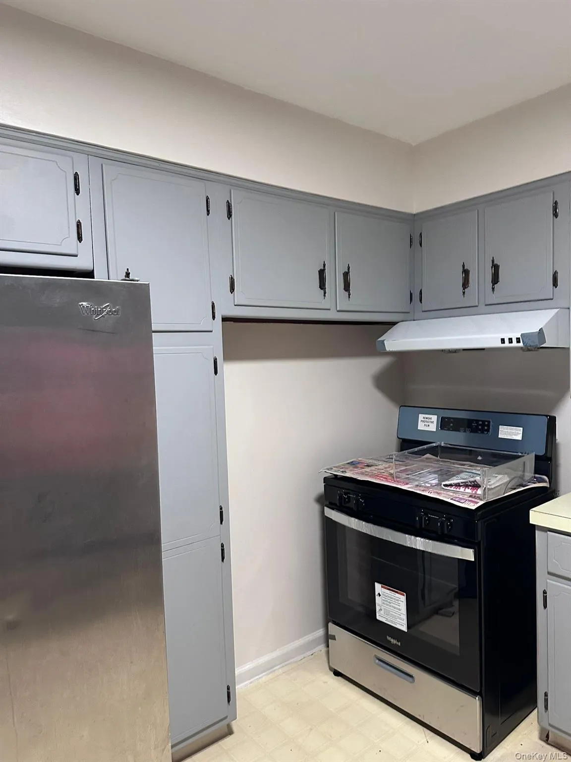 Kitchen with appliances with stainless steel finishes, light floors, under cabinet range hood, light countertops, and gray cabinets Kitchen with appliances with stainless steel finishes, light floors, under cabinet range hood, light countertops, and gray cabinets