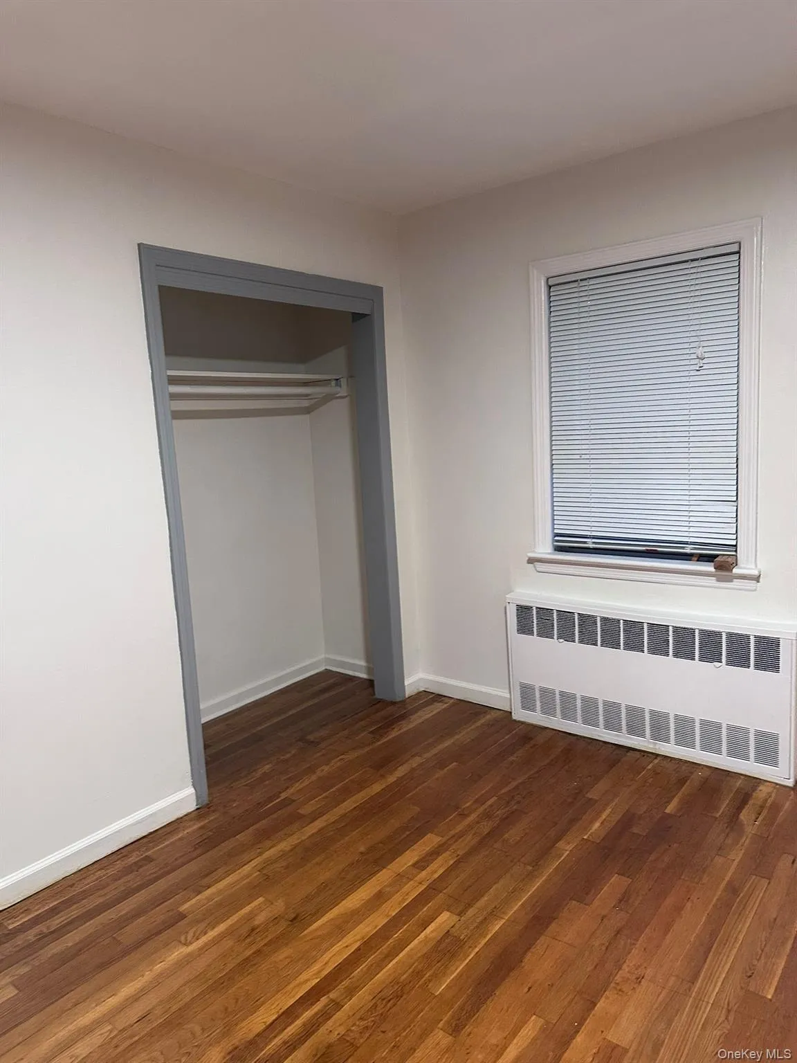 Unfurnished bedroom featuring radiator heating unit, dark wood finished floors, and a closet Unfurnished bedroom featuring radiator heating unit, dark wood finished floors, and a closet