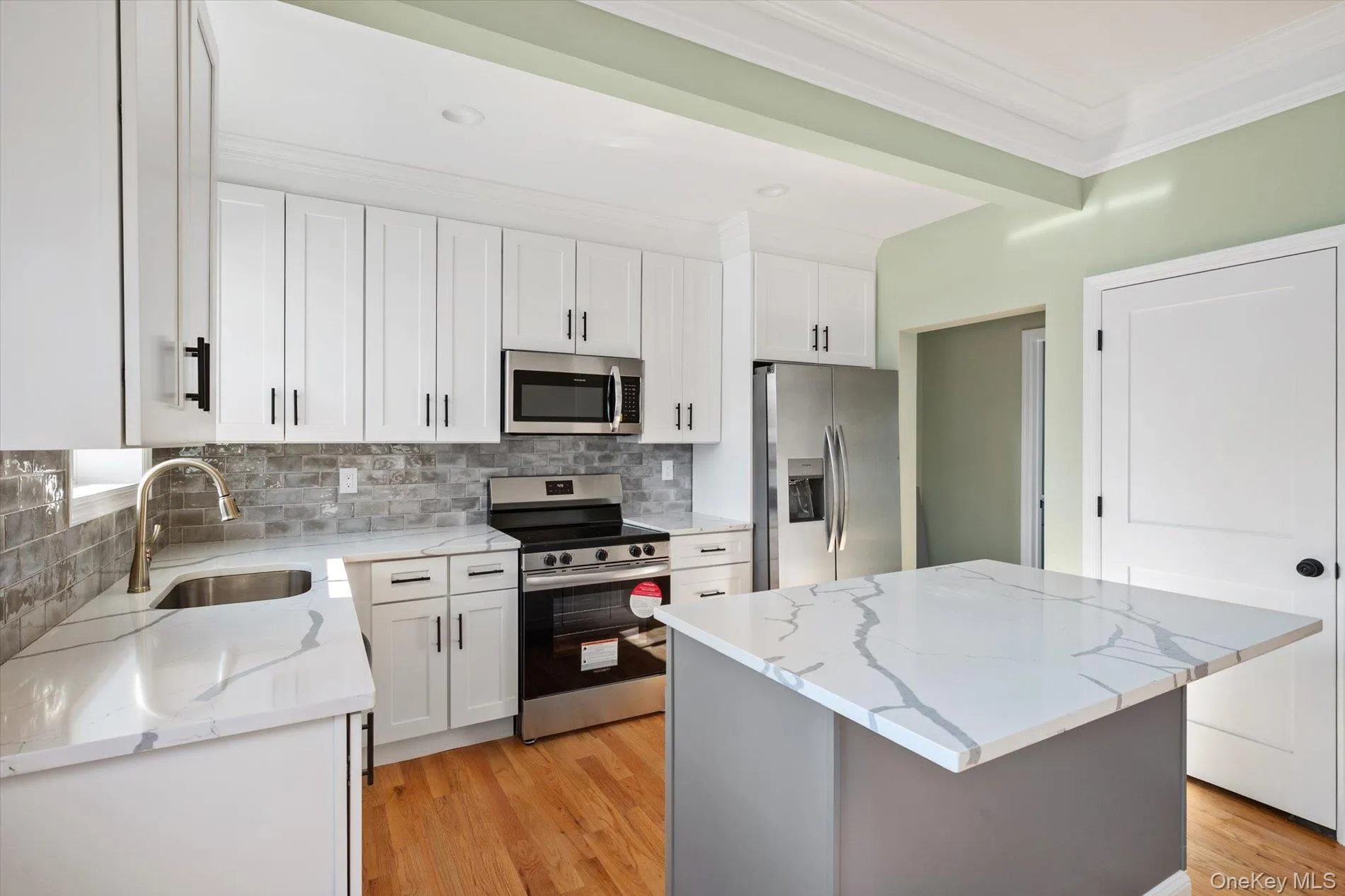 Kitchen featuring stainless steel appliances, white cabinets, a center island, light stone counters, and ornamental molding Kitchen featuring stainless steel appliances, white cabinets, a center island, light stone counters, and ornamental molding