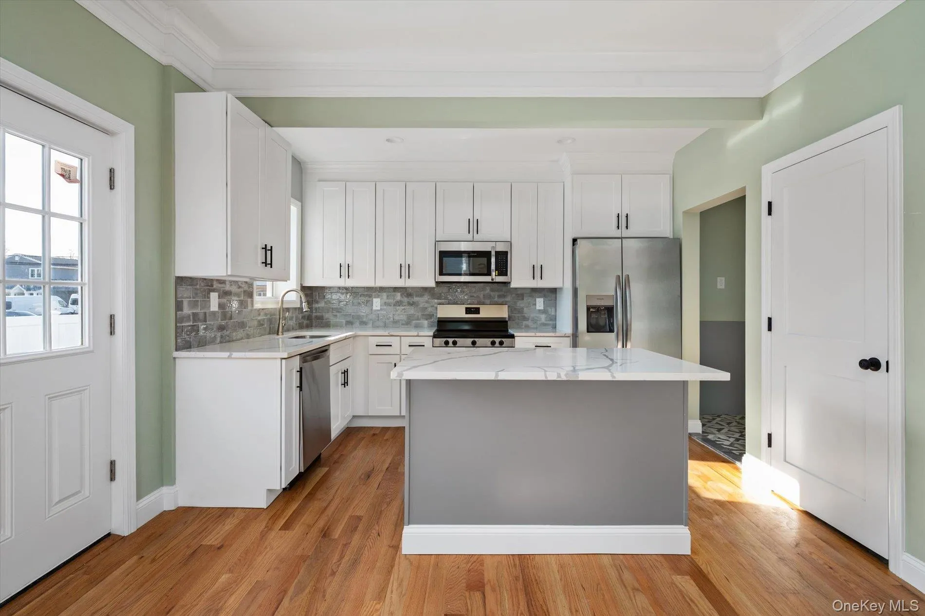 Kitchen featuring light stone countertops, white cabinetry, stainless steel appliances, ornamental molding, and light wood finished floors Kitchen featuring light stone countertops, white cabinetry, stainless steel appliances, ornamental molding, and light wood finished floors