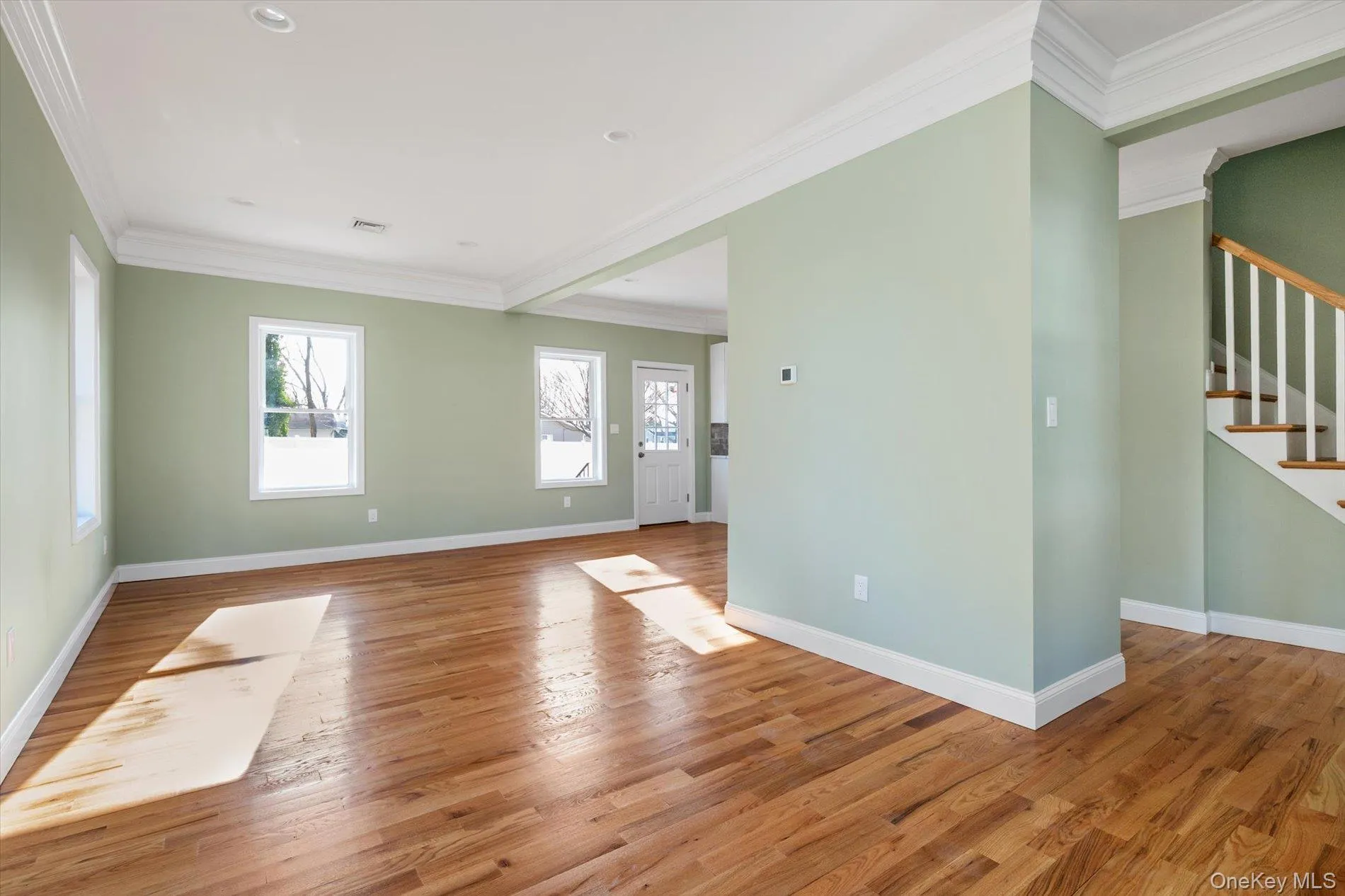 Unfurnished living room with ornamental molding, light wood-style flooring, and stairs Unfurnished living room with ornamental molding, light wood-style flooring, and stairs
