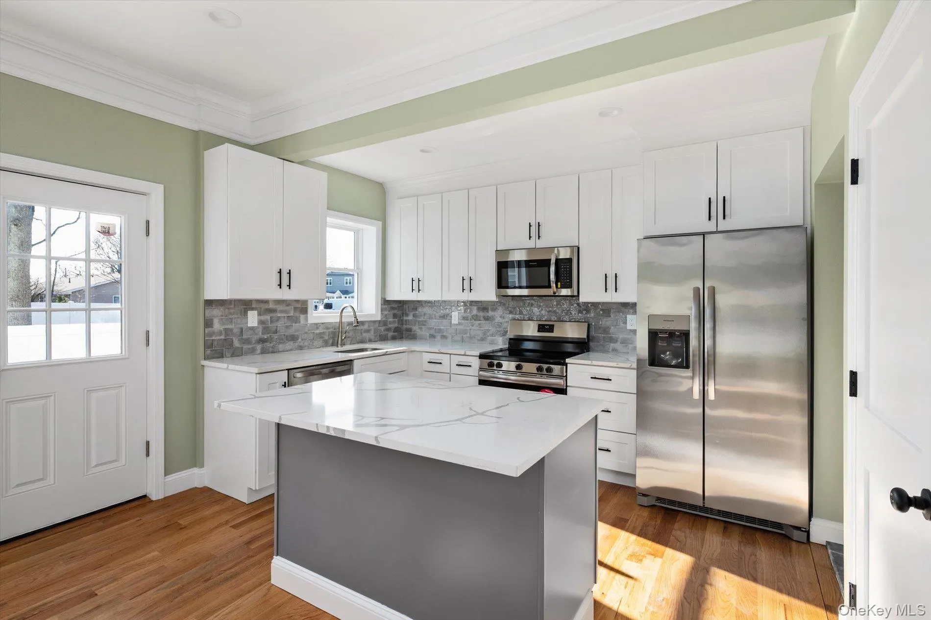 Kitchen featuring appliances with stainless steel finishes, white cabinets, light stone countertops, ornamental molding, and decorative backsplash Kitchen featuring appliances with stainless steel finishes, white cabinets, light stone countertops, ornamental molding, and decorative backsplash
