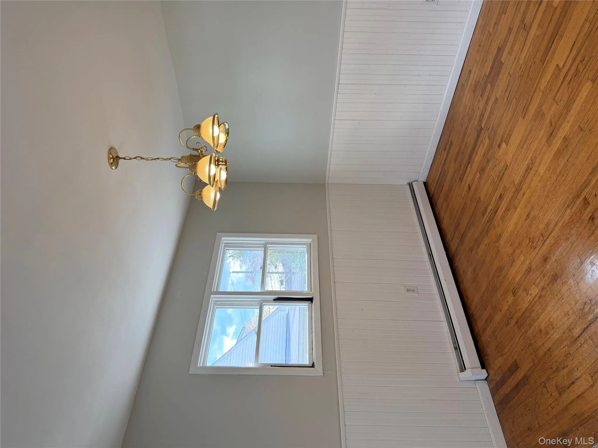Unfurnished room with hardwood / wood-style flooring, a baseboard radiator, wainscoting, and a chandelier Unfurnished room with hardwood / wood-style flooring, a baseboard radiator, wainscoting, and a chandelier