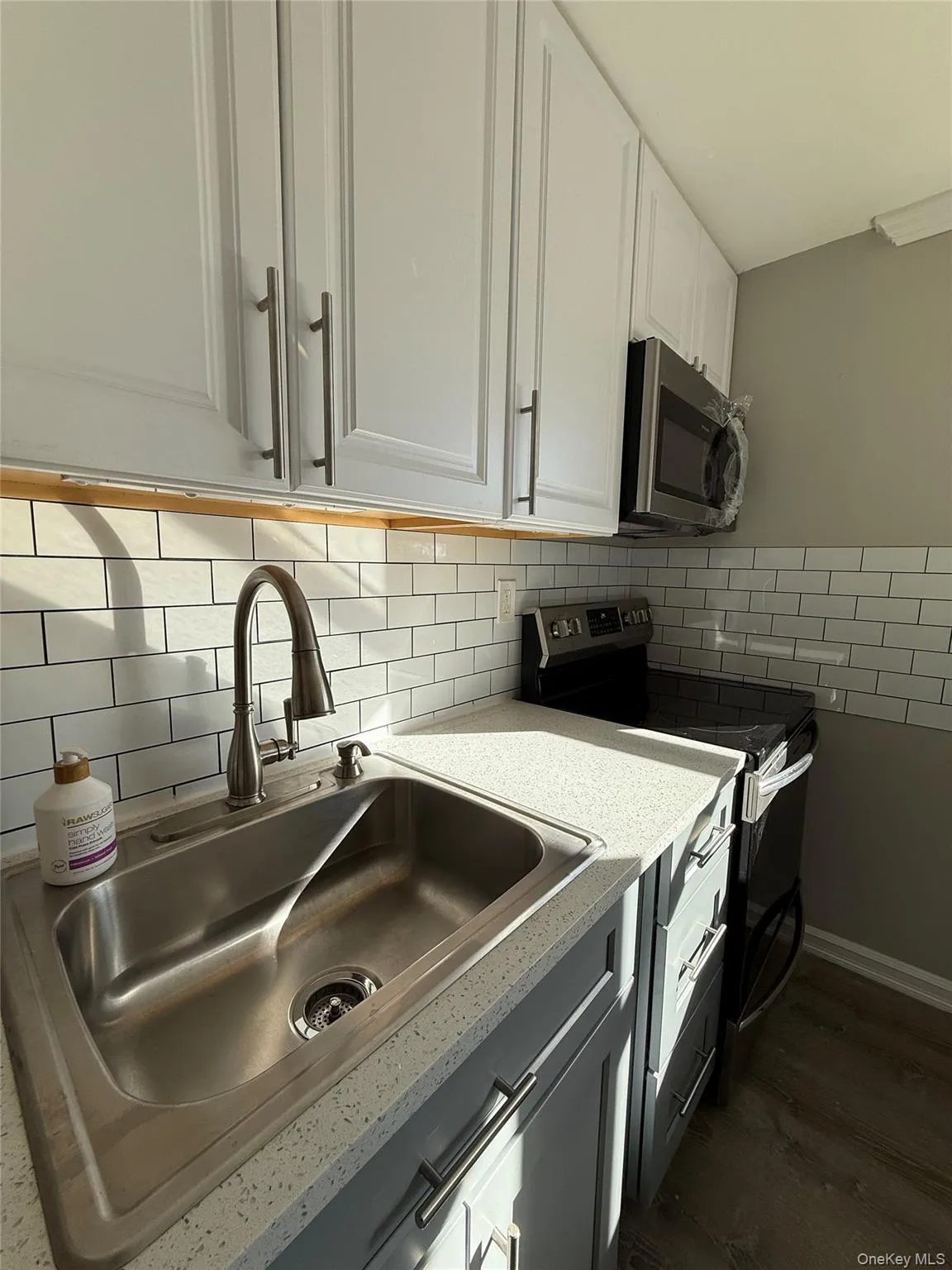 Kitchen with appliances with stainless steel finishes, white cabinetry, tasteful backsplash, dark wood finished floors, and light stone countertops Kitchen with appliances with stainless steel finishes, white cabinetry, tasteful backsplash, dark wood finished floors, and light stone countertops