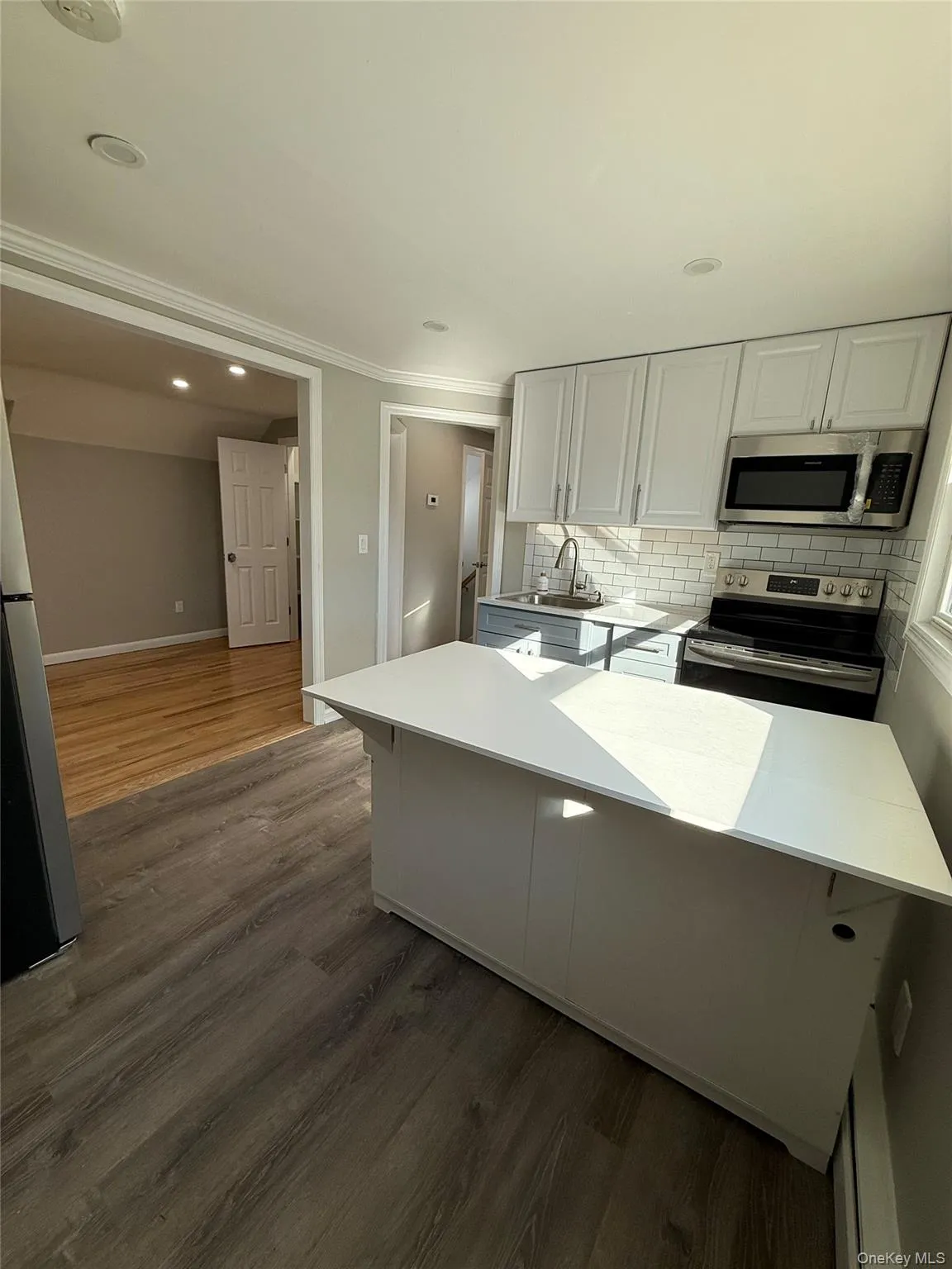 Kitchen with appliances with stainless steel finishes, backsplash, dark wood-style flooring, white cabinetry, and recessed lighting Kitchen with appliances with stainless steel finishes, backsplash, dark wood-style flooring, white cabinetry, and recessed lighting
