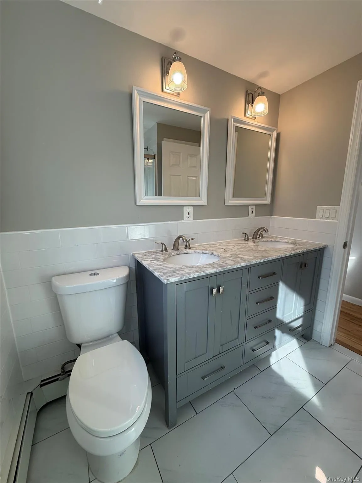 Bathroom featuring double vanity, a wainscoted wall, a baseboard radiator, and tile walls Bathroom featuring double vanity, a wainscoted wall, a baseboard radiator, and tile walls
