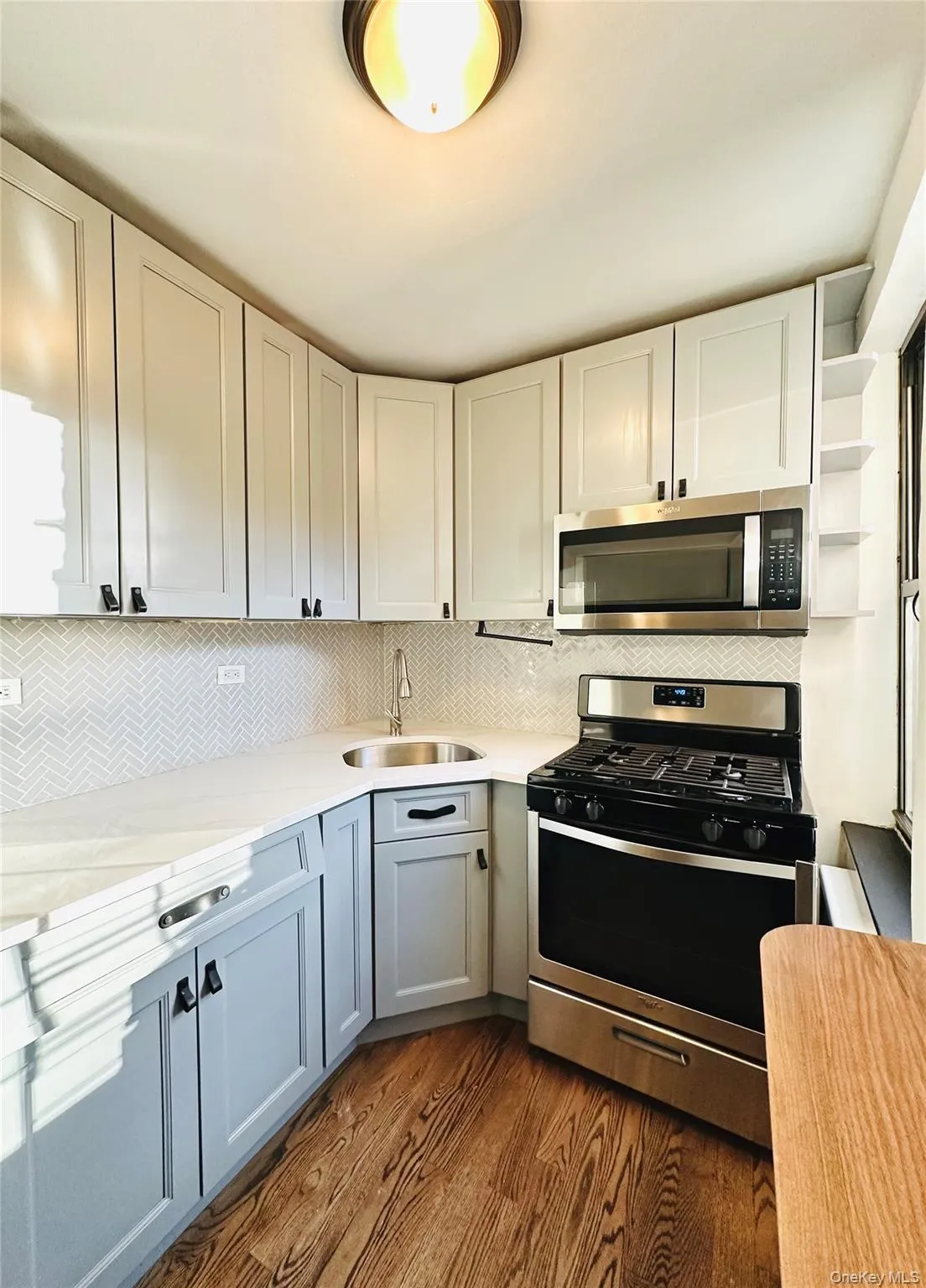 Kitchen with stainless steel appliances, backsplash, dark wood finished floors, white cabinets, and light stone counters Kitchen with stainless steel appliances, backsplash, dark wood finished floors, white cabinets, and light stone counters