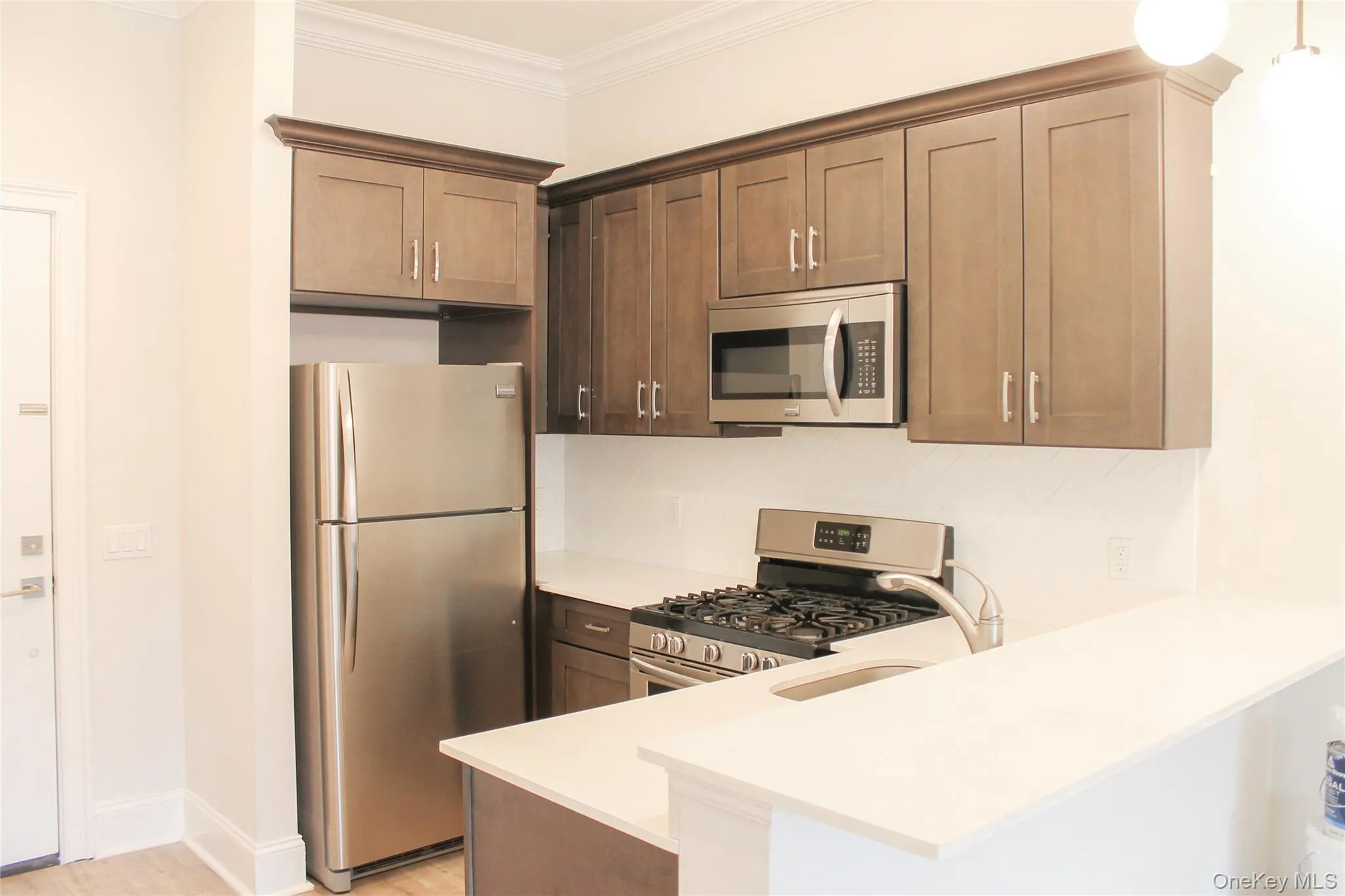 Kitchen featuring appliances with stainless steel finishes, crown molding, light wood finished floors, a peninsula, and decorative backsplash Kitchen featuring appliances with stainless steel finishes, crown molding, light wood finished floors, a peninsula, and decorative backsplash