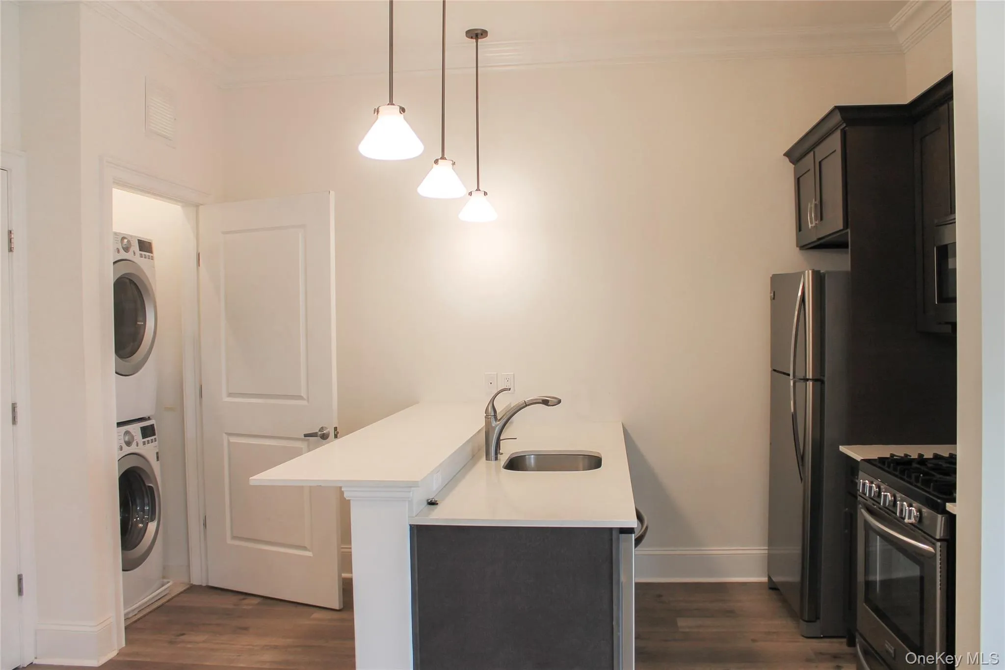 Washroom featuring crown molding, dark wood-style flooring, and stacked washing machine and dryer Washroom featuring crown molding, dark wood-style flooring, and stacked washing machine and dryer