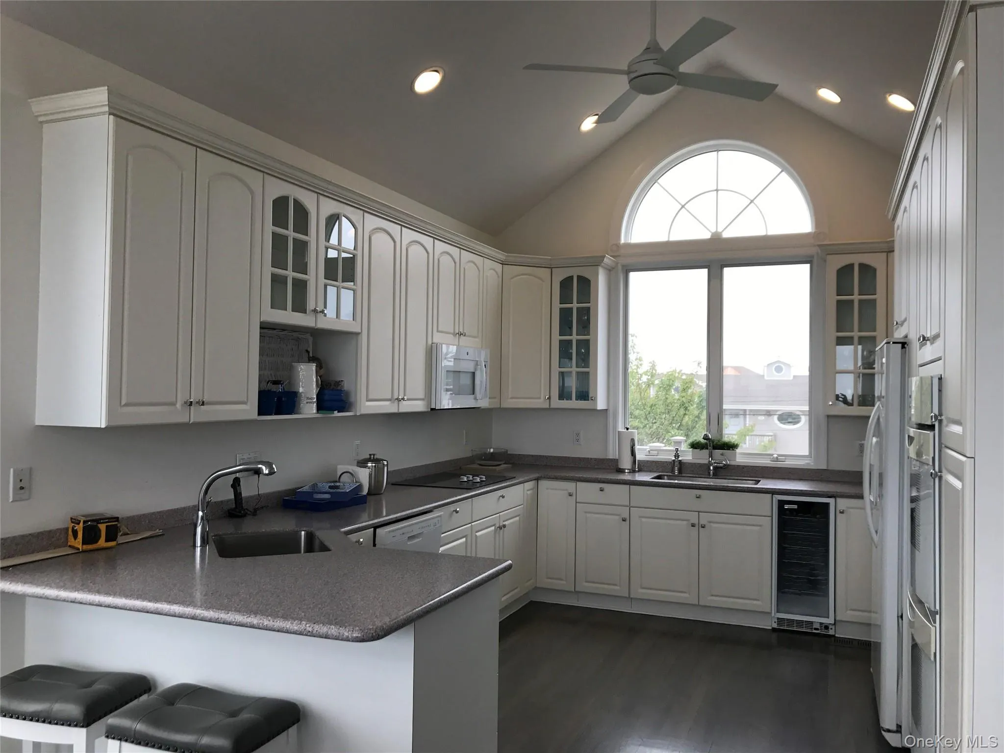 Kitchen featuring glass insert cabinets, a peninsula, vaulted ceiling, white cabinets, and wine cooler Kitchen featuring glass insert cabinets, a peninsula, vaulted ceiling, white cabinets, and wine cooler