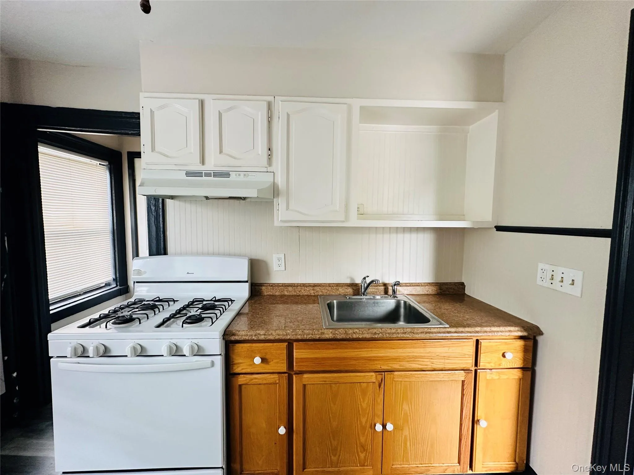 Kitchen featuring white gas stove, dark countertops, under cabinet range hood, open shelves, and white cabinets Kitchen featuring white gas stove, dark countertops, under cabinet range hood, open shelves, and white cabinets