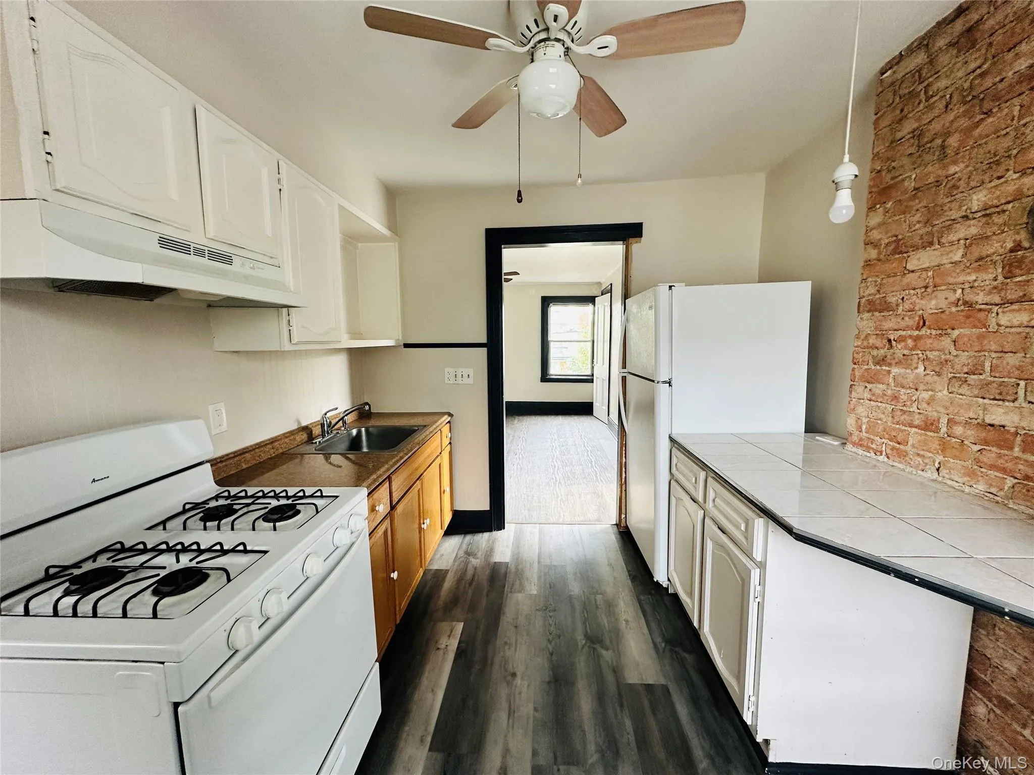 Kitchen with white appliances, brick wall, white cabinets, under cabinet range hood, and tile countertops Kitchen with white appliances, brick wall, white cabinets, under cabinet range hood, and tile countertops