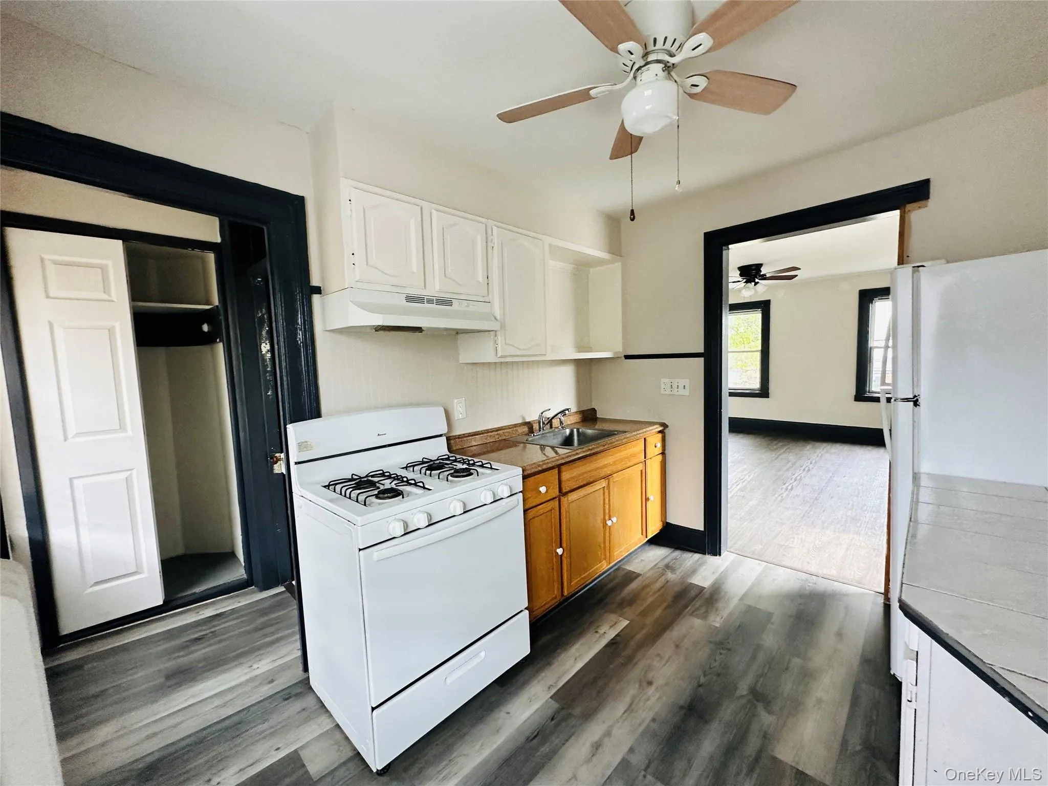 Kitchen with white appliances, white cabinets, dark wood-type flooring, under cabinet range hood, and light countertops Kitchen with white appliances, white cabinets, dark wood-type flooring, under cabinet range hood, and light countertops
