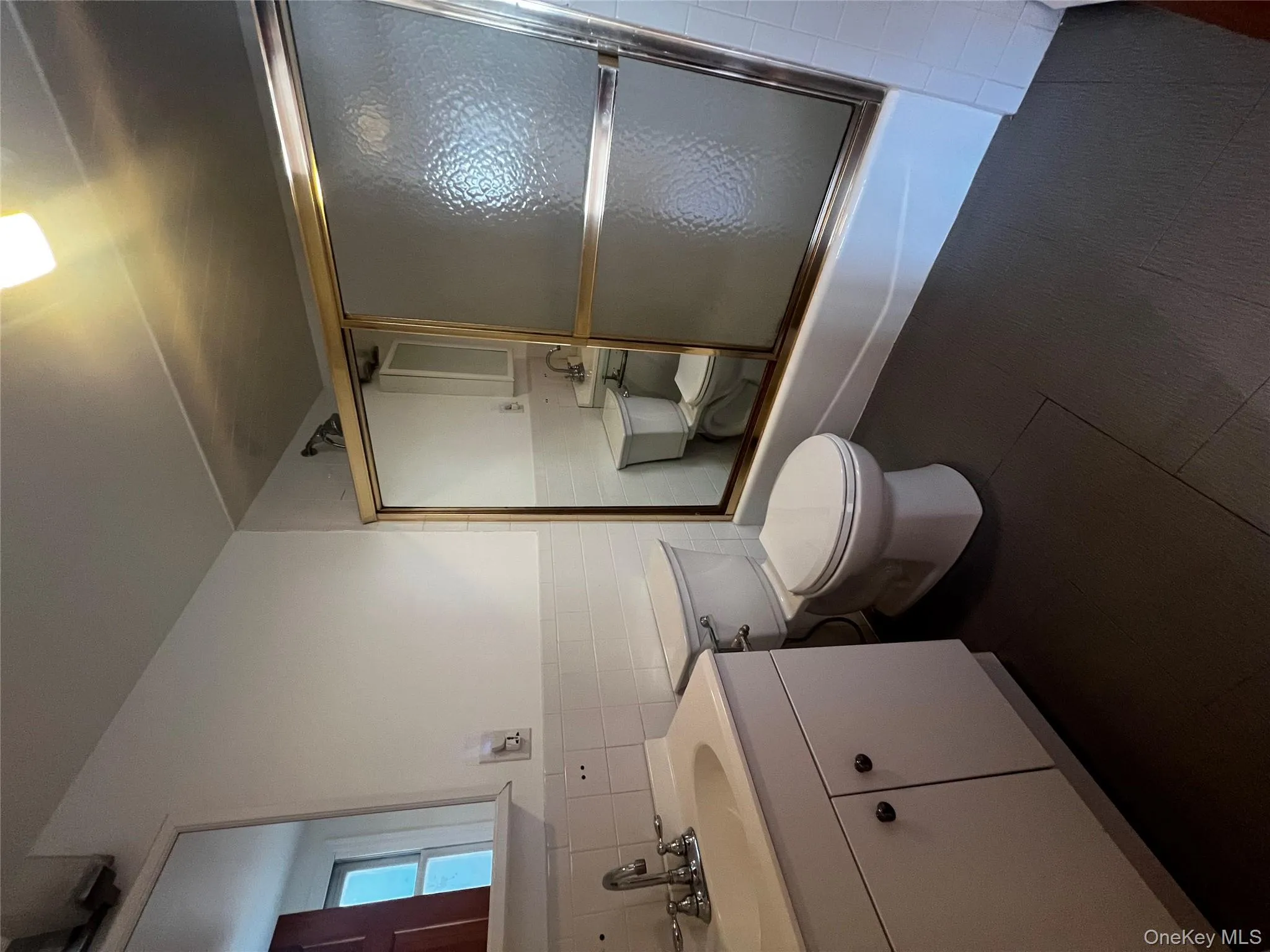 Full bath featuring vanity, tile walls, shower / bath combination with glass door, a wainscoted wall, and dark tile patterned floors Full bath featuring vanity, tile walls, shower / bath combination with glass door, a wainscoted wall, and dark tile patterned floors