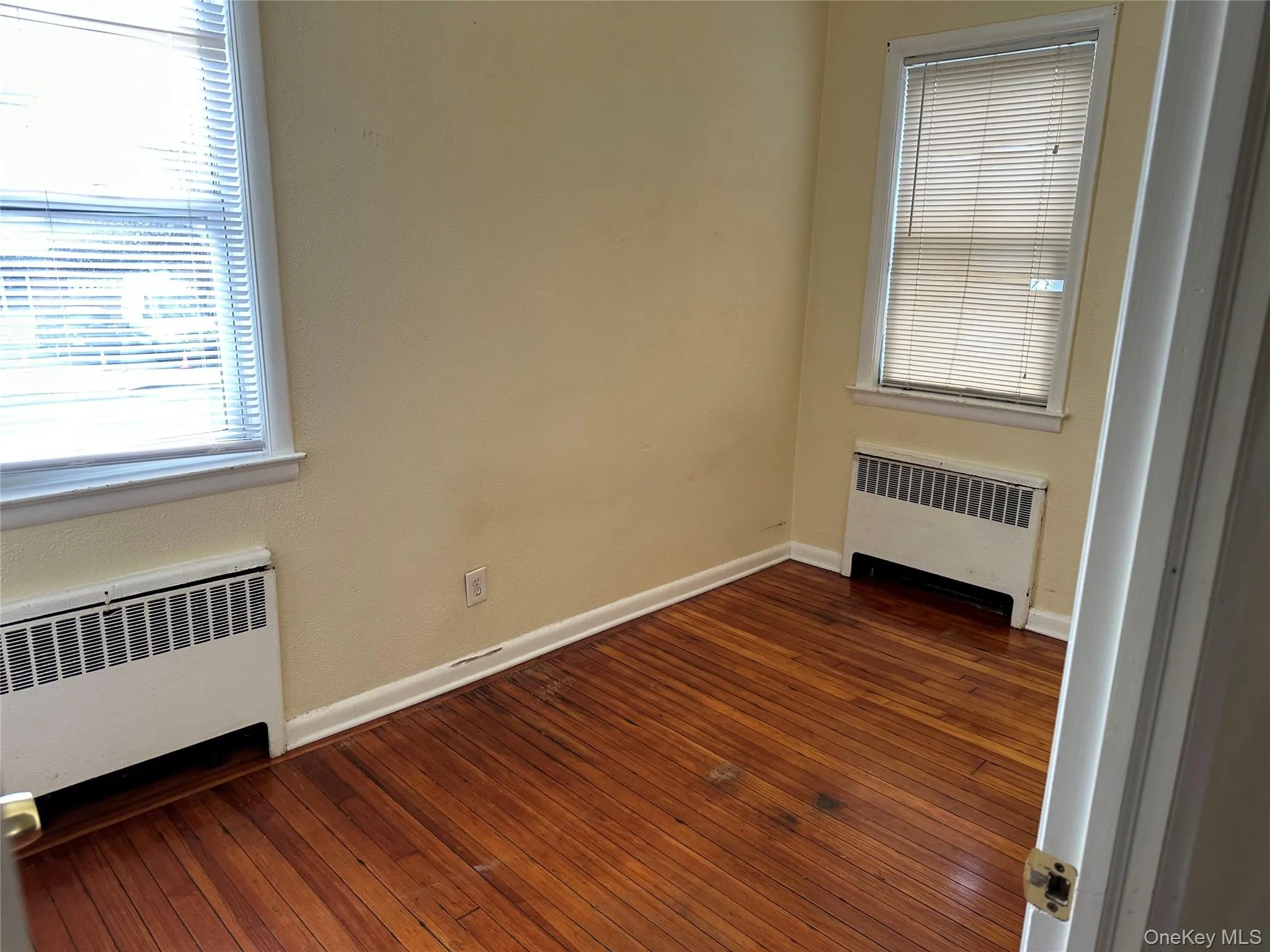 Empty room with radiator, dark wood-type flooring, and plenty of natural light Empty room with radiator, dark wood-type flooring, and plenty of natural light