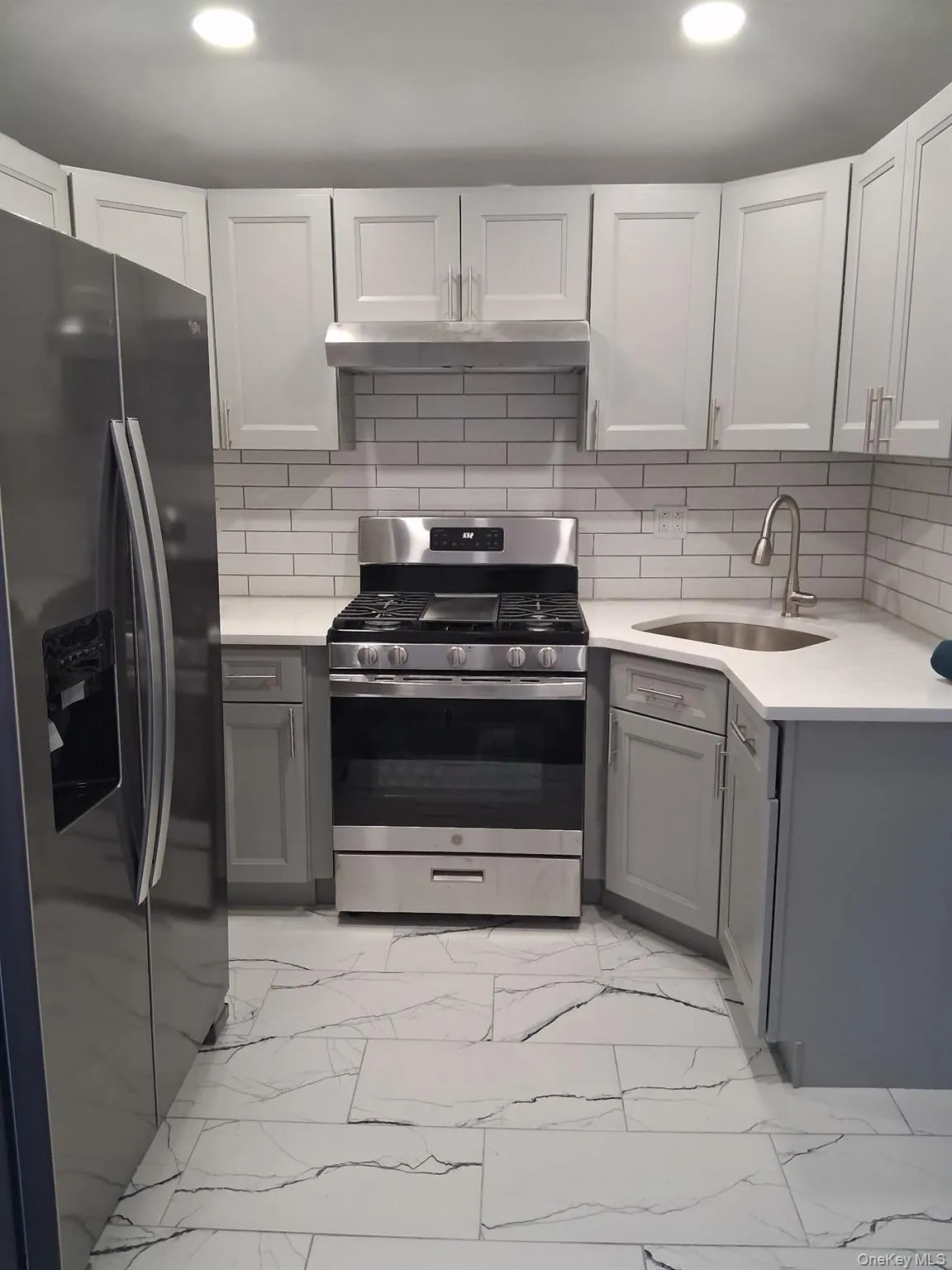 Kitchen featuring appliances with stainless steel finishes, light marble finish flooring, backsplash, gray cabinetry, and recessed lighting Kitchen featuring appliances with stainless steel finishes, light marble finish flooring, backsplash, gray cabinetry, and recessed lighting