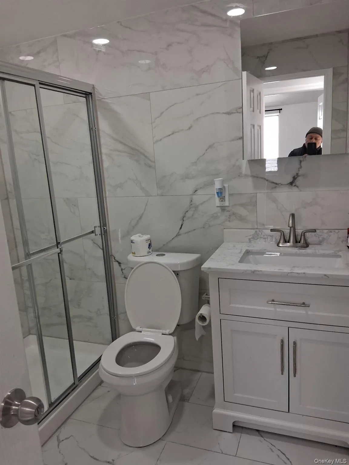 Bathroom with a marble finish shower, tile walls, vanity, and light marble finish flooring Bathroom with a marble finish shower, tile walls, vanity, and light marble finish flooring