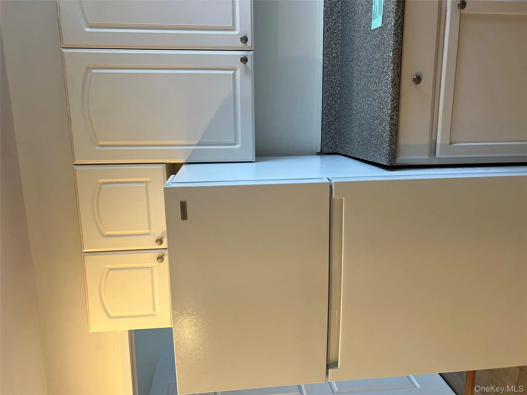 Kitchen with white fridge, dark countertops, and white cabinets Kitchen with white fridge, dark countertops, and white cabinets