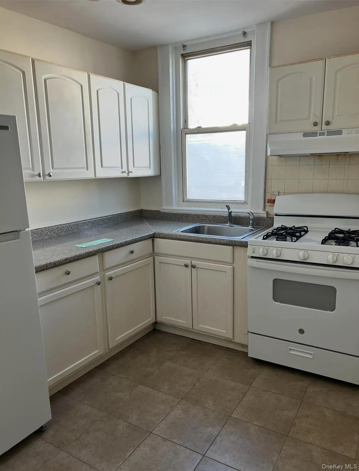 Kitchen featuring white appliances, white cabinetry, under cabinet range hood, and dark countertops Kitchen featuring white appliances, white cabinetry, under cabinet range hood, and dark countertops