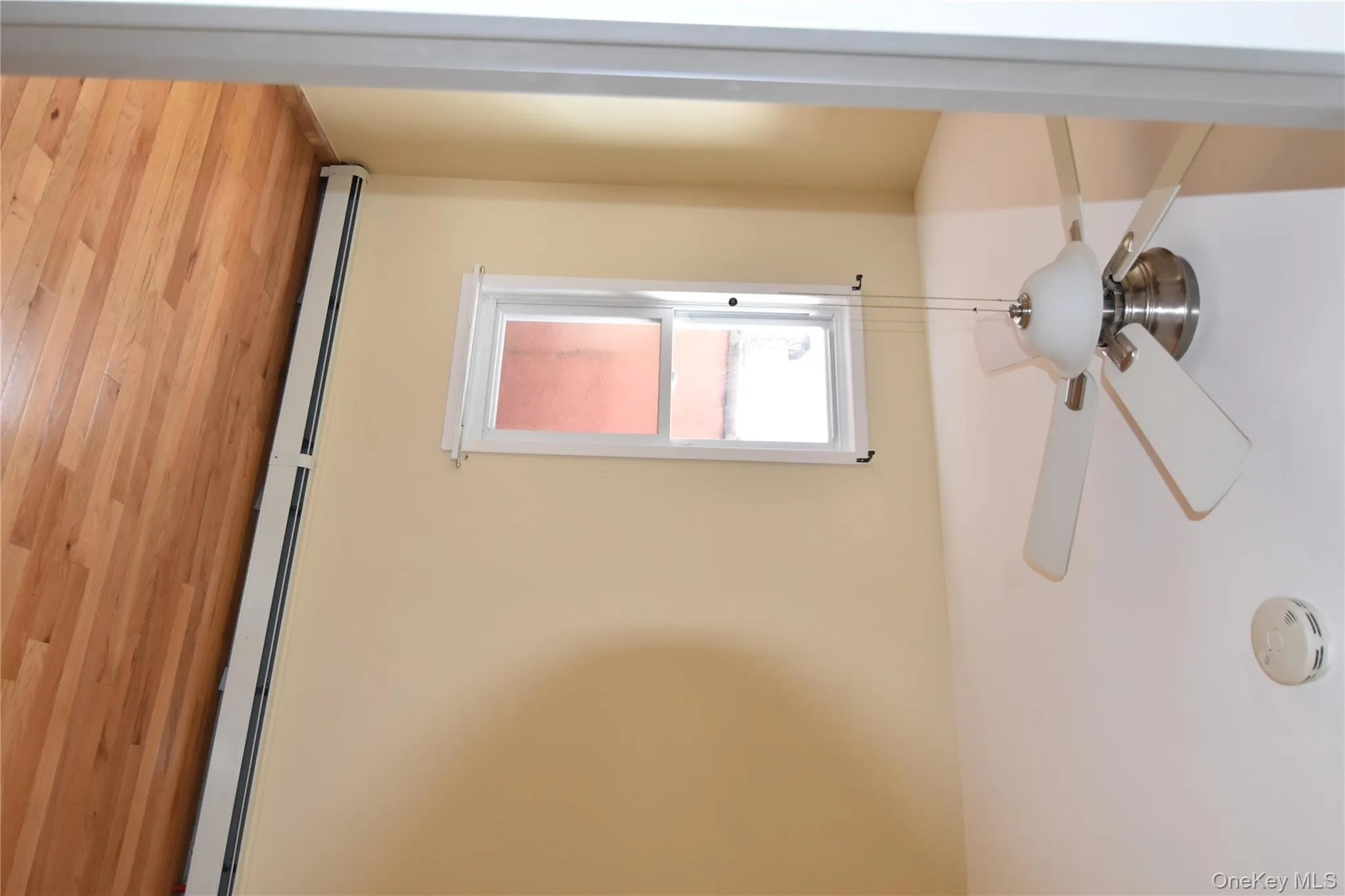 Unfurnished room featuring a baseboard radiator, light wood-type flooring, a ceiling fan, and a smoke detector Unfurnished room featuring a baseboard radiator, light wood-type flooring, a ceiling fan, and a smoke detector