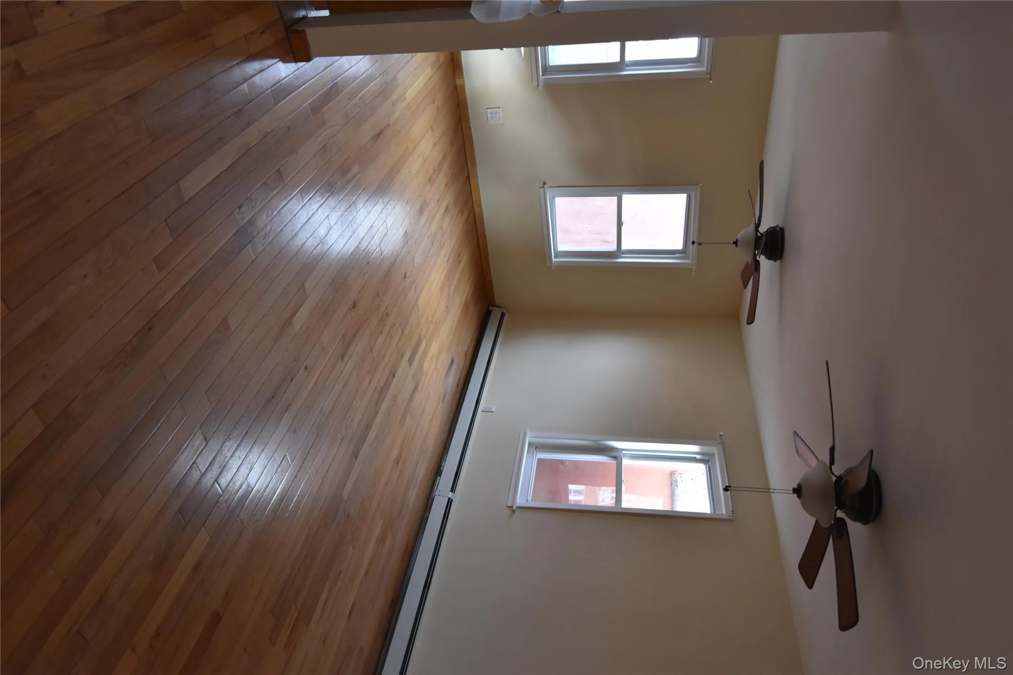 Empty room with baseboard heating, light wood-type flooring, and ceiling fan Empty room with baseboard heating, light wood-type flooring, and ceiling fan