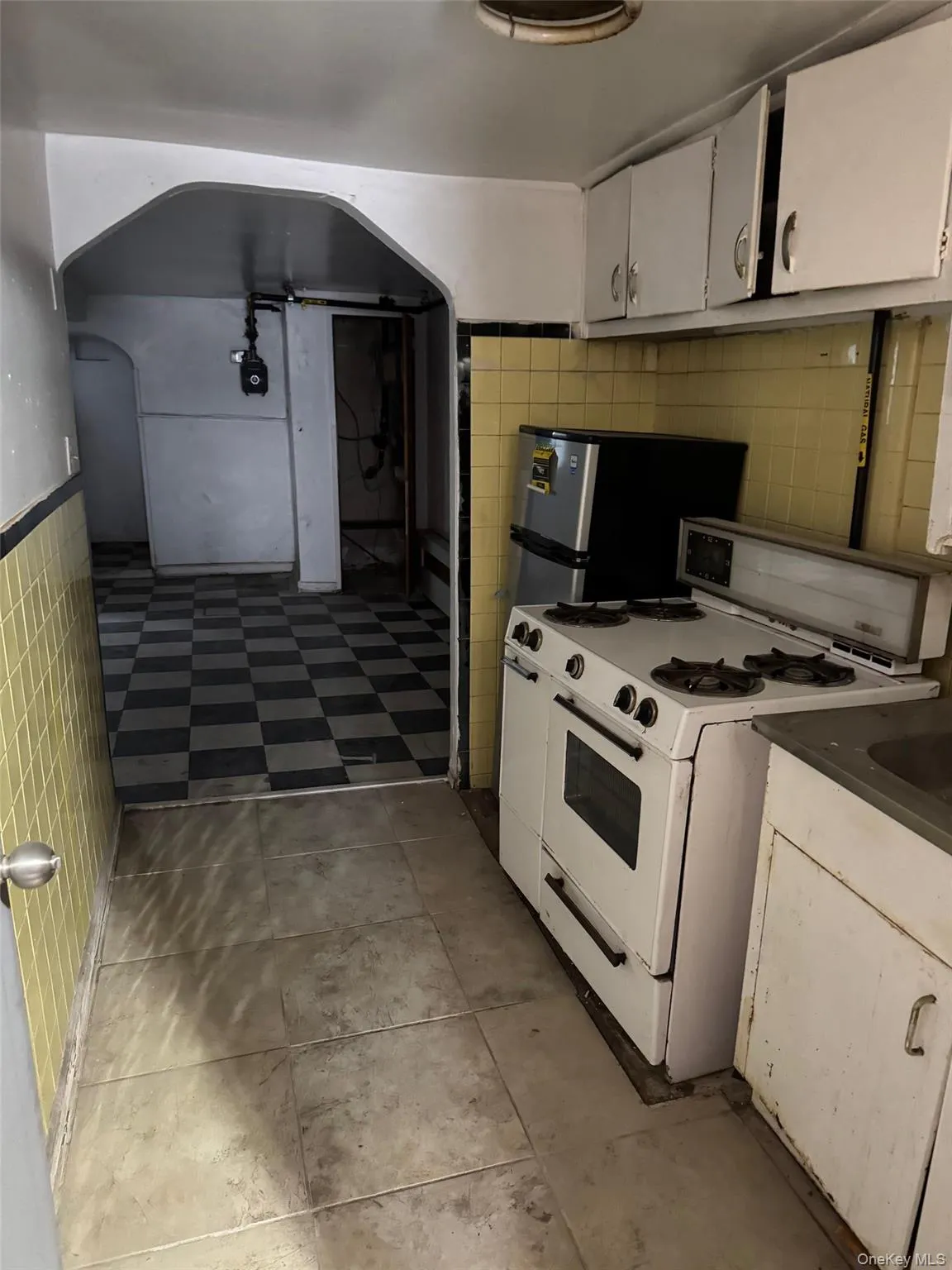 Kitchen with white range with gas cooktop, tile walls, white cabinetry, a wainscoted wall, and freestanding refrigerator Kitchen with white range with gas cooktop, tile walls, white cabinetry, a wainscoted wall, and freestanding refrigerator