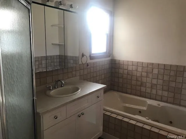 Full bathroom featuring vanity, a whirlpool tub, tile walls, and a shower with door Full bathroom featuring vanity, a whirlpool tub, tile walls, and a shower with door