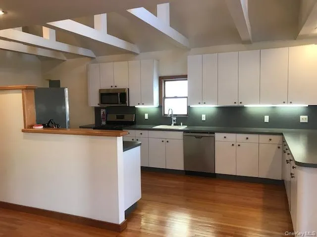 Kitchen with white cabinets, stainless steel appliances, light wood-style flooring, dark countertops, and a peninsula Kitchen with white cabinets, stainless steel appliances, light wood-style flooring, dark countertops, and a peninsula