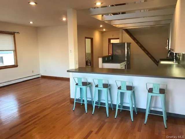 Kitchen with dark wood-style flooring, freestanding refrigerator, a kitchen breakfast bar, dark countertops, and a peninsula Kitchen with dark wood-style flooring, freestanding refrigerator, a kitchen breakfast bar, dark countertops, and a peninsula
