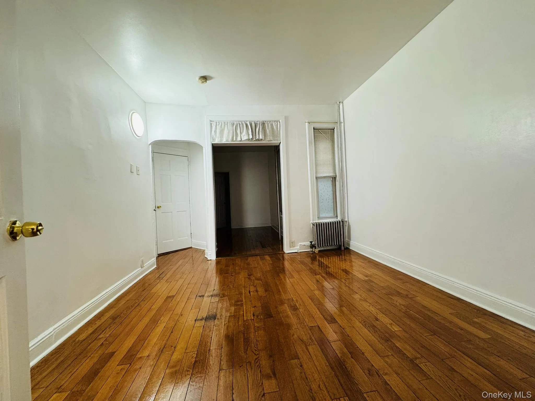 Unfurnished room with arched walkways, hardwood / wood-style flooring, and radiator Unfurnished room with arched walkways, hardwood / wood-style flooring, and radiator