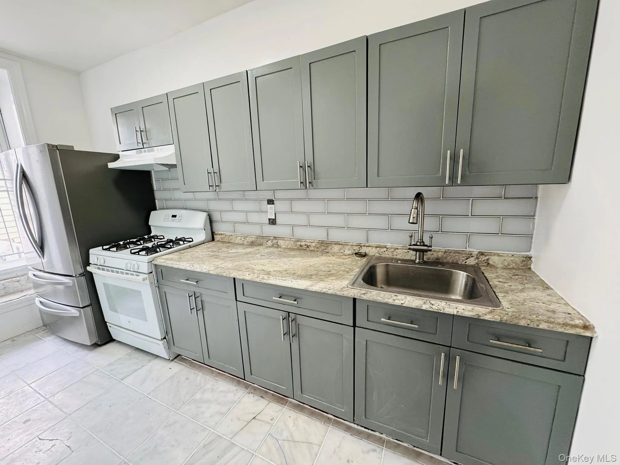 Kitchen featuring gray cabinetry, decorative backsplash, white range with gas cooktop, and freestanding refrigerator Kitchen featuring gray cabinetry, decorative backsplash, white range with gas cooktop, and freestanding refrigerator