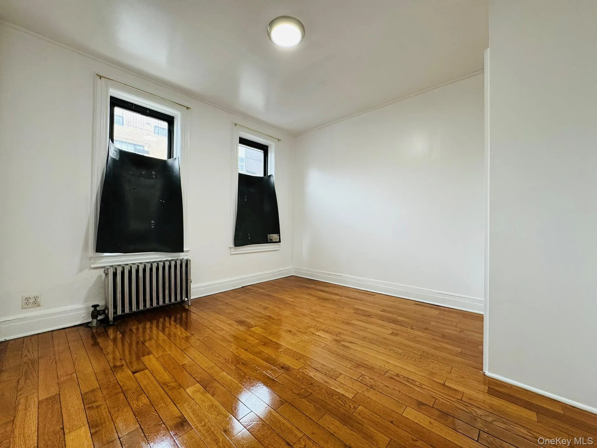 Unfurnished room featuring radiator heating unit, hardwood / wood-style floors, and ornamental molding Unfurnished room featuring radiator heating unit, hardwood / wood-style floors, and ornamental molding