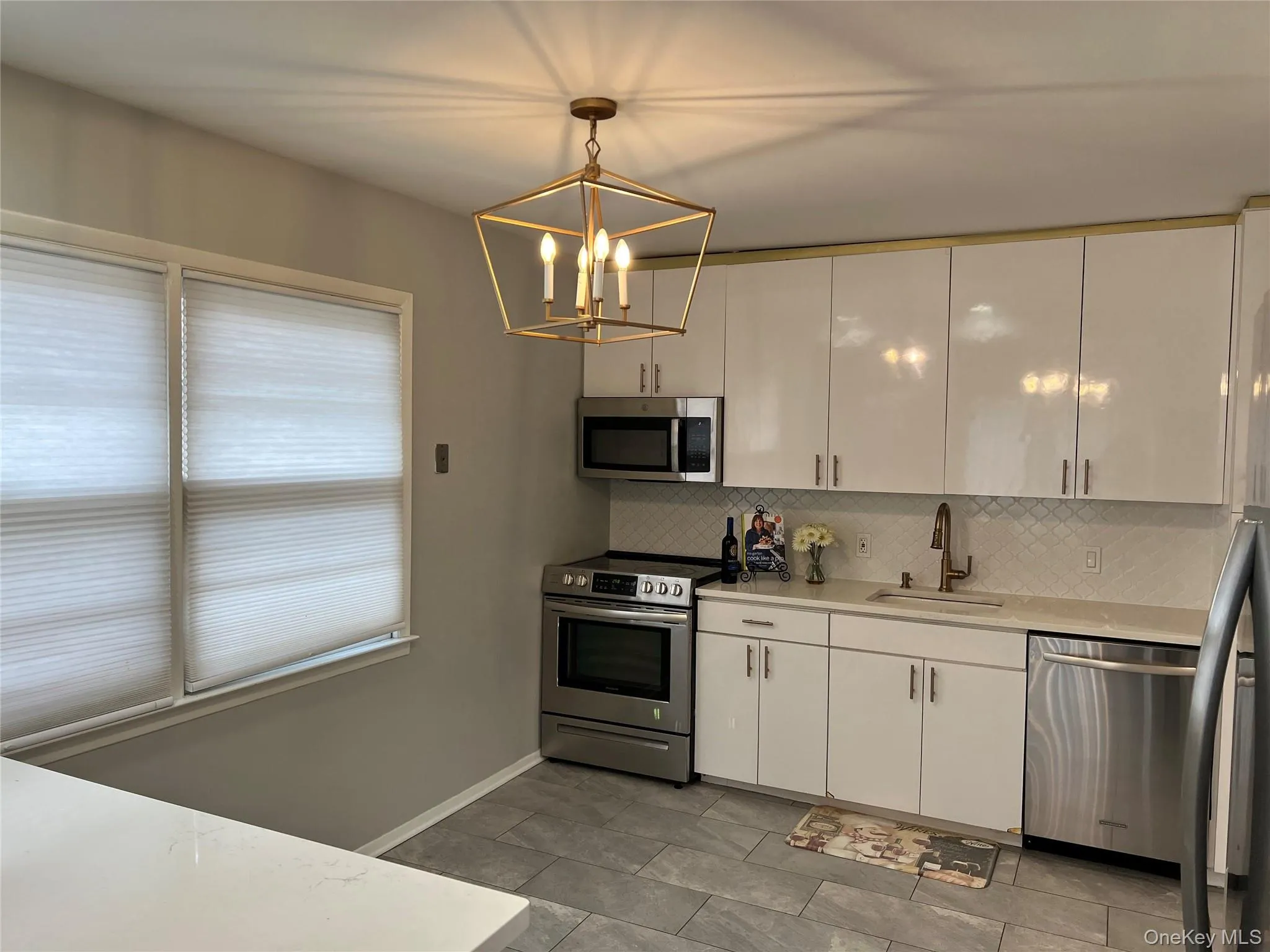 Kitchen featuring appliances with stainless steel finishes, decorative backsplash, pendant lighting, and white cabinetry Kitchen featuring appliances with stainless steel finishes, decorative backsplash, pendant lighting, and white cabinetry