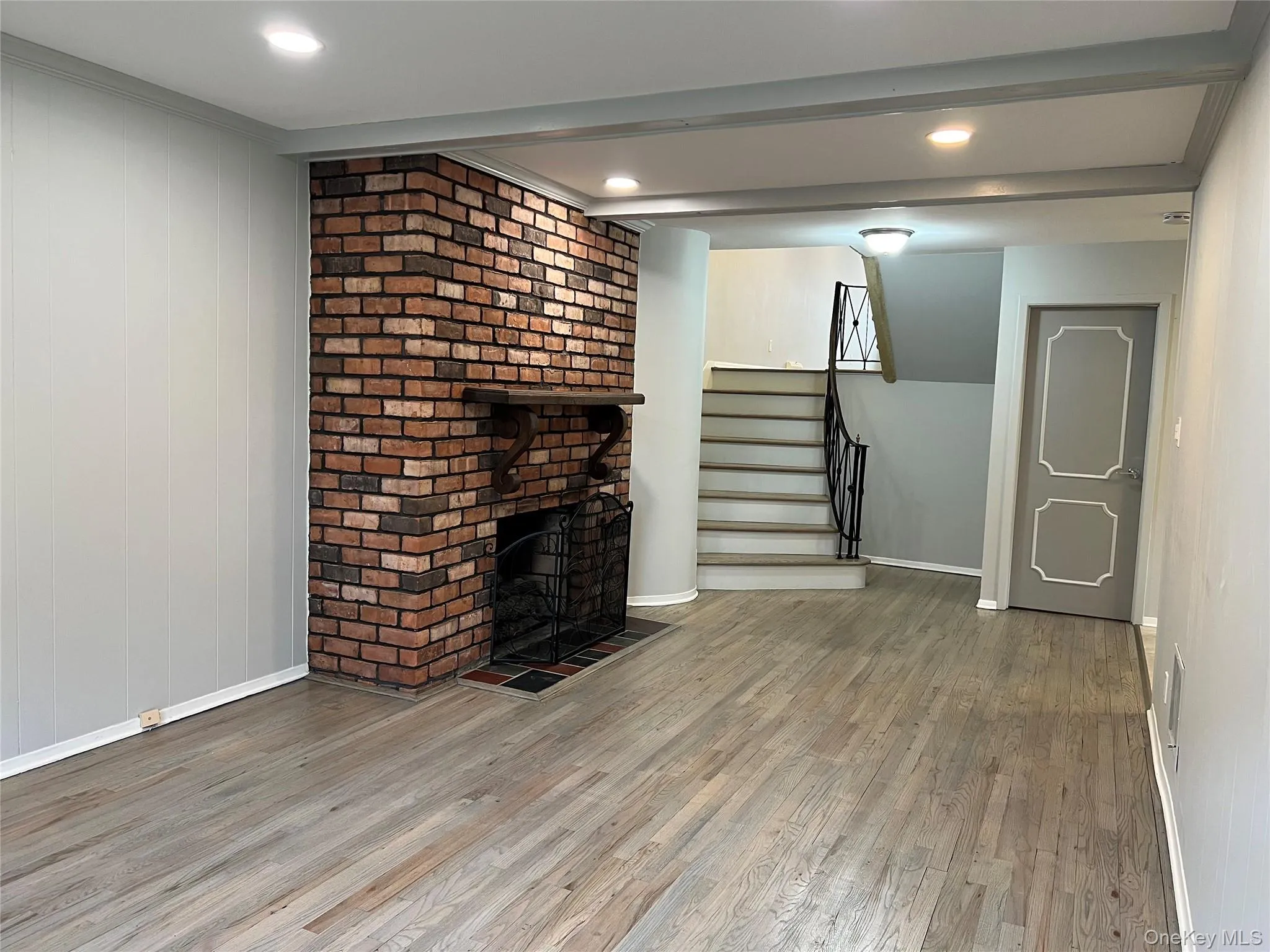 Unfurnished Den featuring wood finished floors, a brick fireplace, stairs, wood walls, and recessed lighting Unfurnished Den featuring wood finished floors, a brick fireplace, stairs, wood walls, and recessed lighting